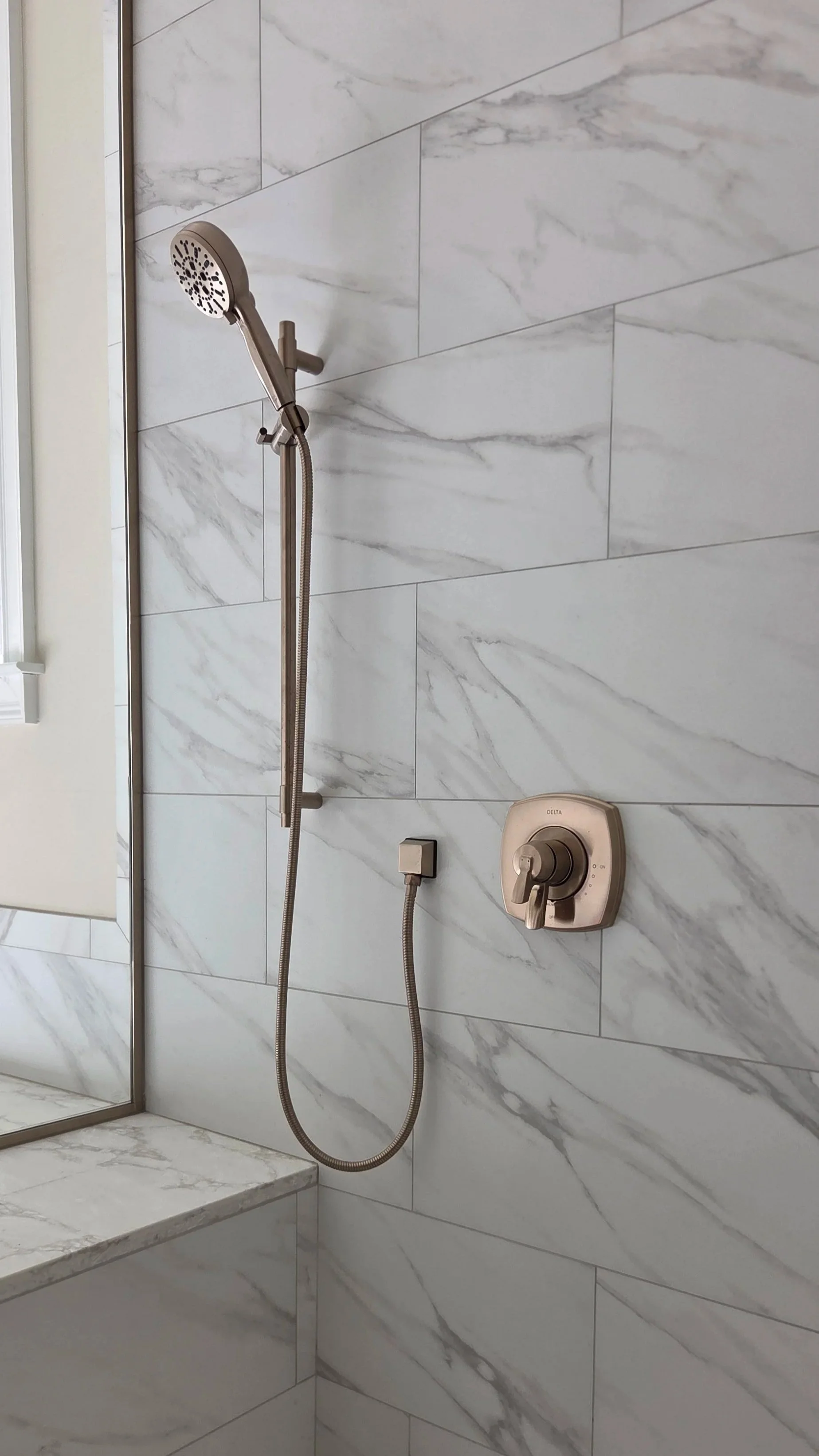 Shower area with marble tiles, a handheld showerhead, and controls.