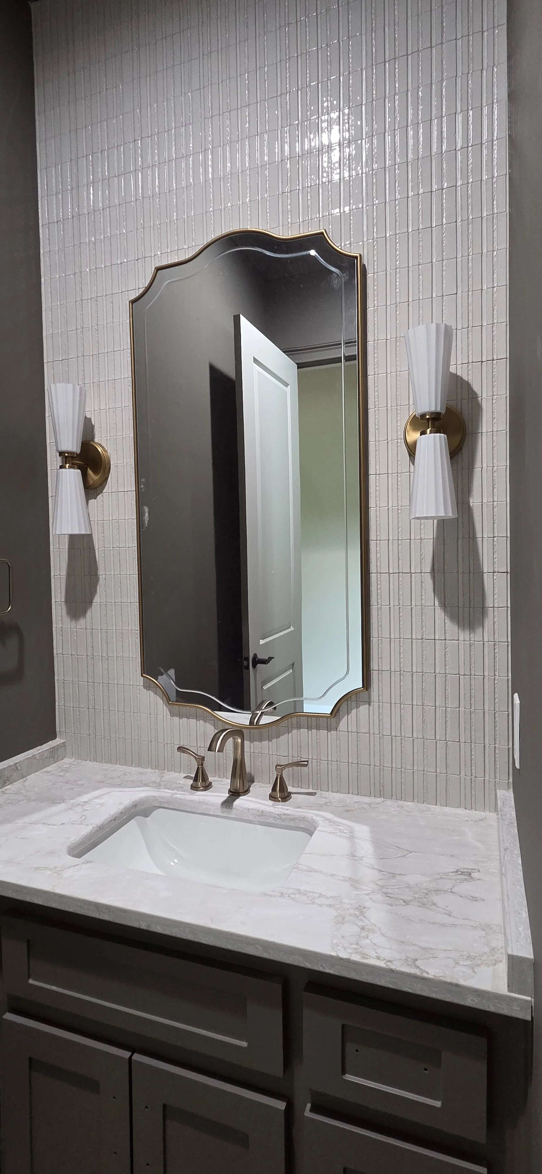 Bathroom vanity with a marble countertop, an undermount sink, brushed gold faucet, a large ornate mirror, and wall sconces with white shades.