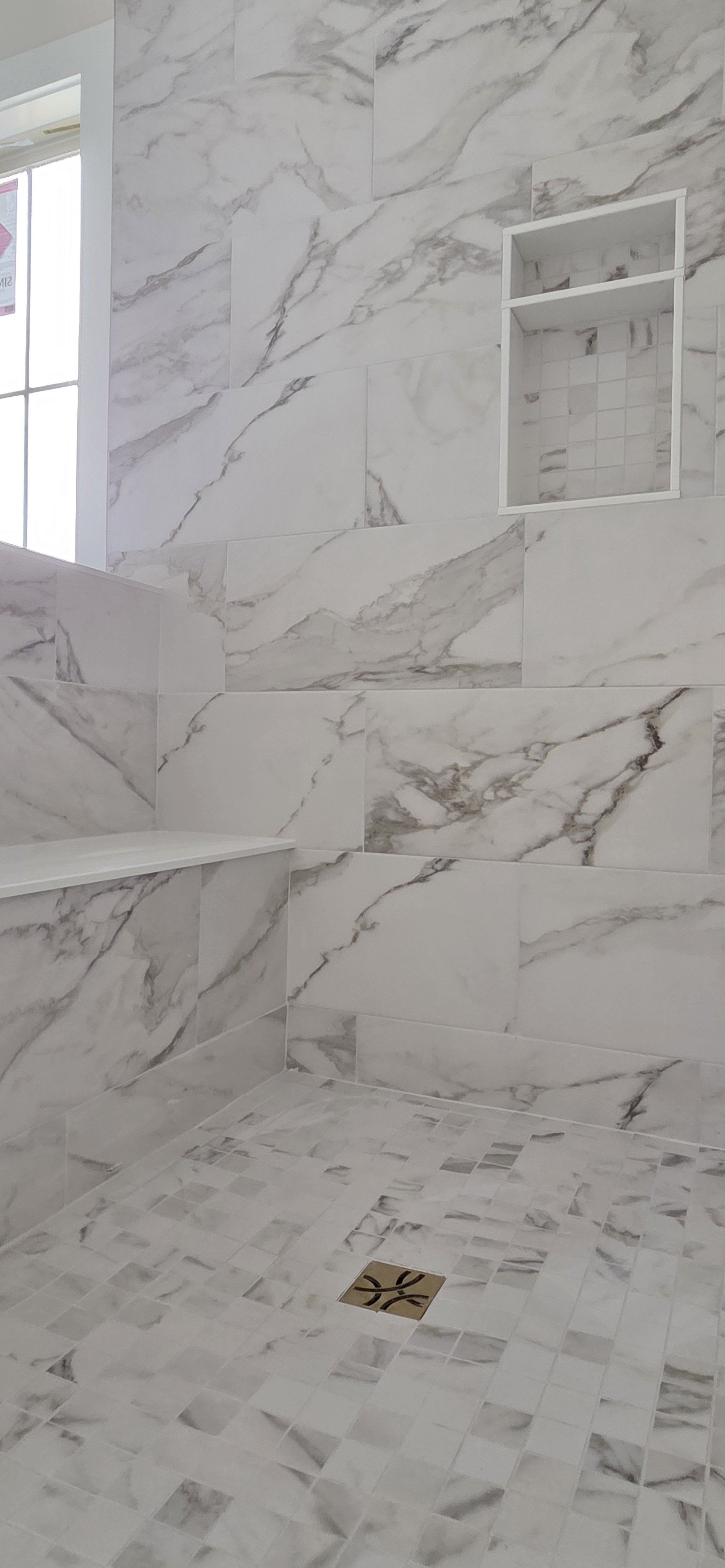 Marble-tiled shower with built-in niche and a small window, featuring a floor drain.