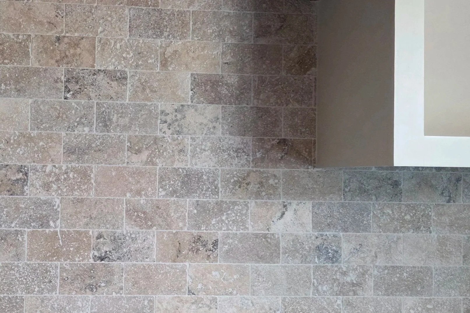 Close-up of a wall made of rectangular stone tiles in shades of gray and beige, with some white speckling.