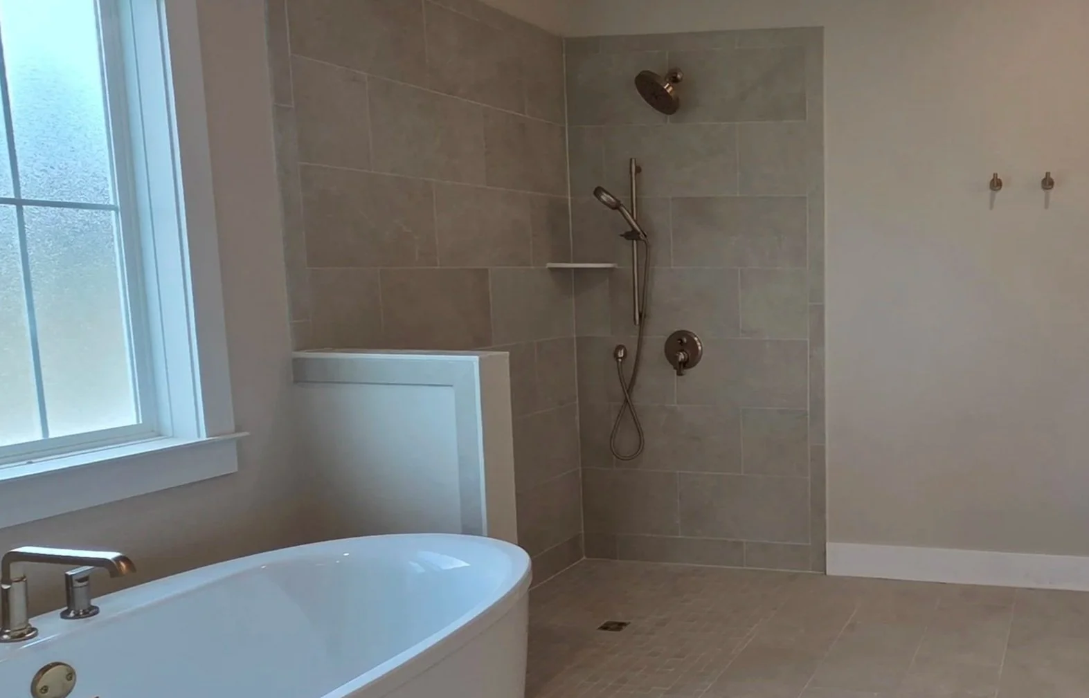 A modern bathroom with a bathtub, a window, and a tiled walk-in shower with a handheld showerhead and a shelf inside.