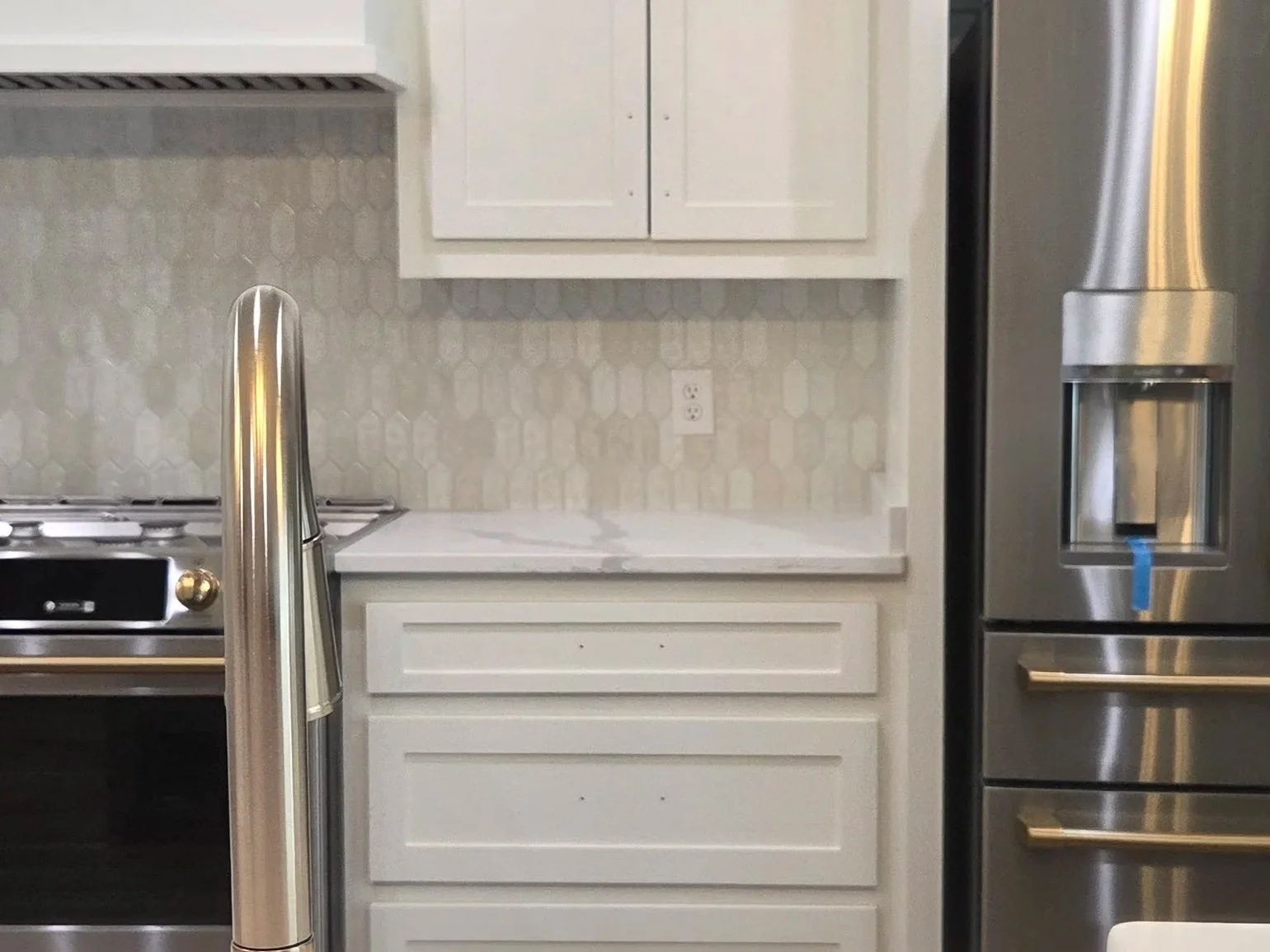 Kitchen with white cabinets, a marble countertop, stainless steel refrigerator, gas stove, and a sink with a curved faucet.