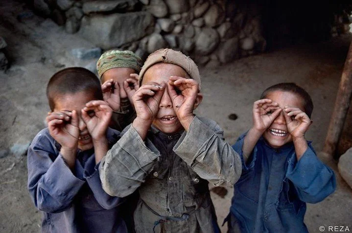 Photograph by Reza Deghati

Four children, hands cupped into makeshift binoculars, peer back at the camera with unguarded, gap-toothed grins. It's a small, playful gesture, but it captures something Reza has spent his entire career chasing: the momen