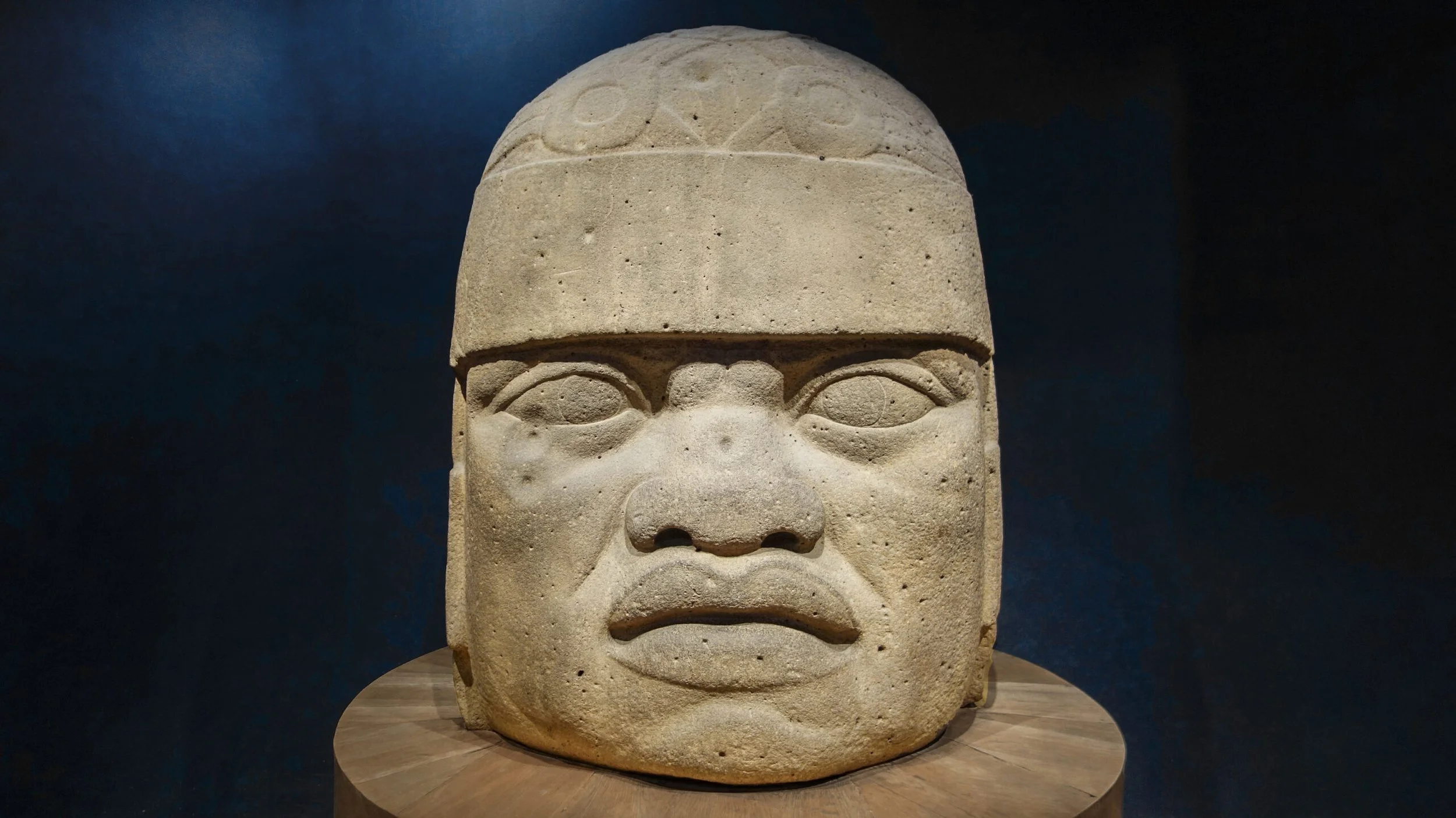"Colossal stone Olmec head with flattened features and a fitted helmet"