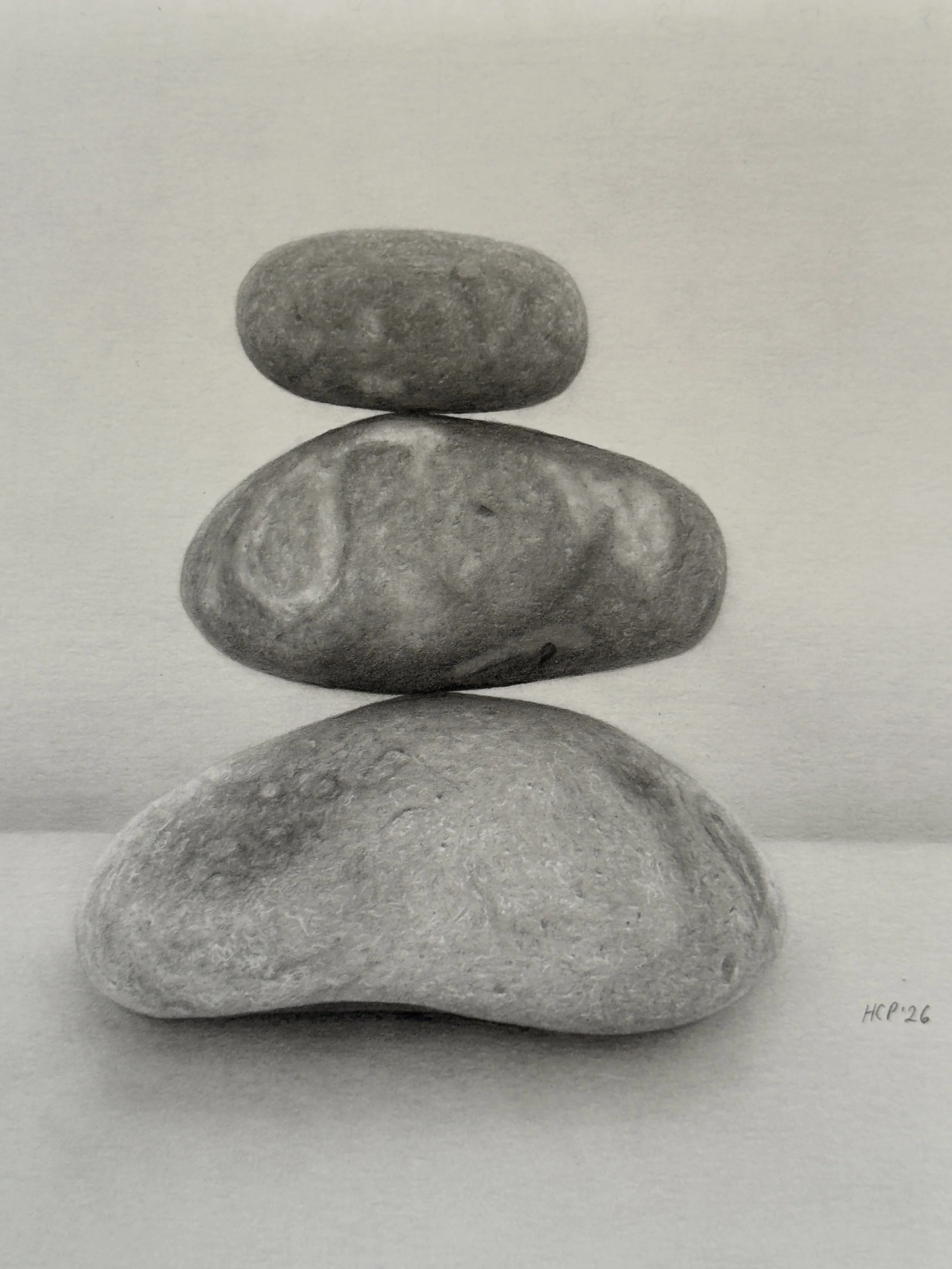 A black and white photograph of five stacked smooth stones arranged in a vertical line on a plain surface with a light background. The bottom stone is the largest and the top stone is the smallest. 