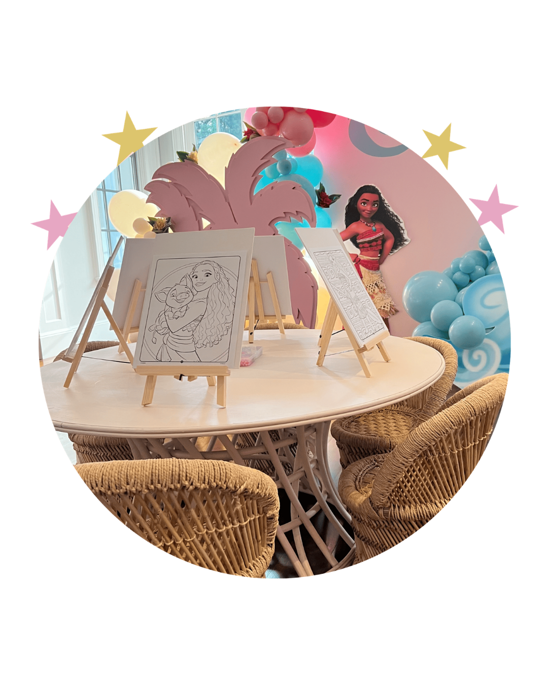 Decorative table with coloring pages, tropical leaves, and Moana character cutout for a child's birthday party.