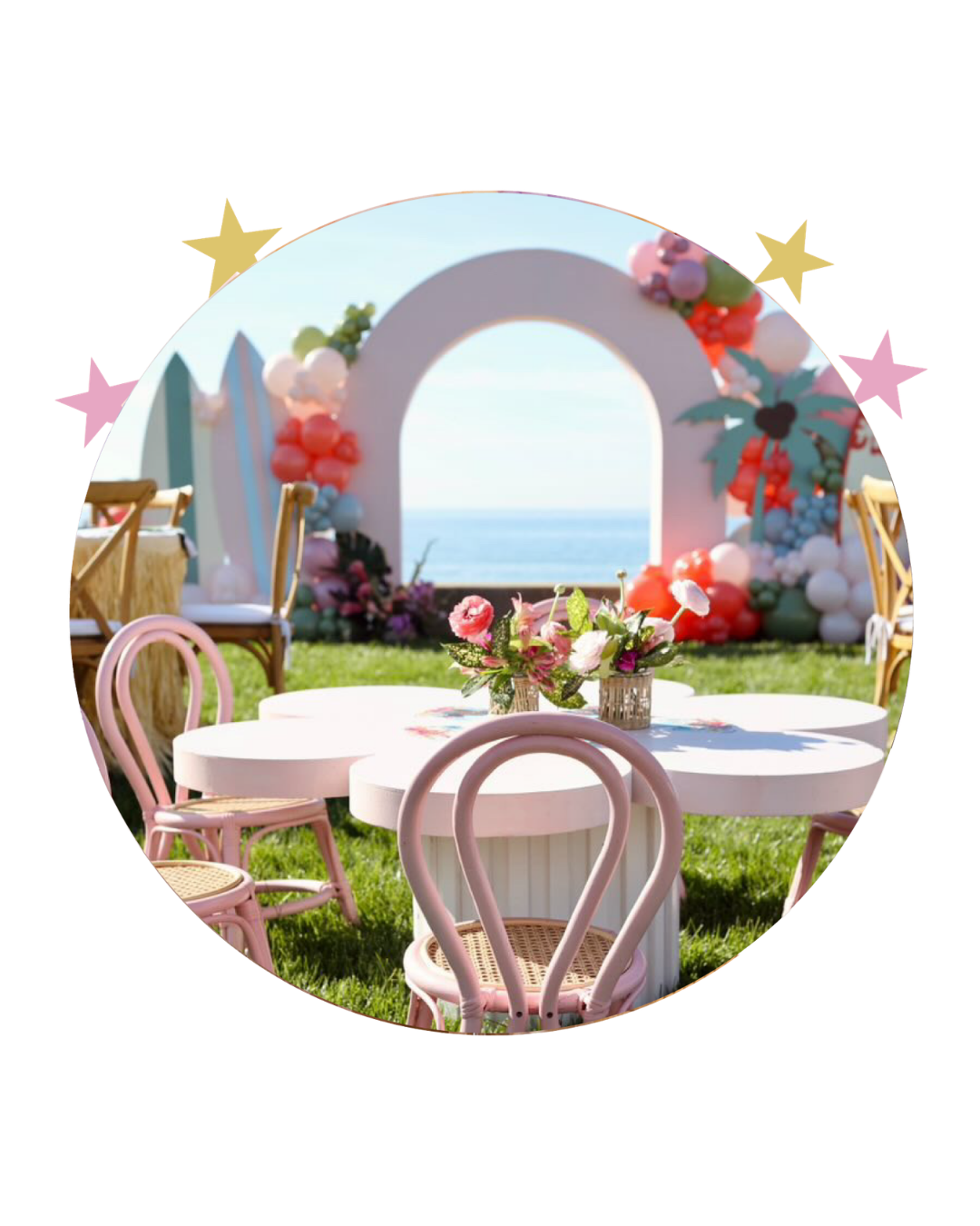 Decorated outdoor event setup with a white arch, balloon arrangements, pink chairs, and a sea view in the background.