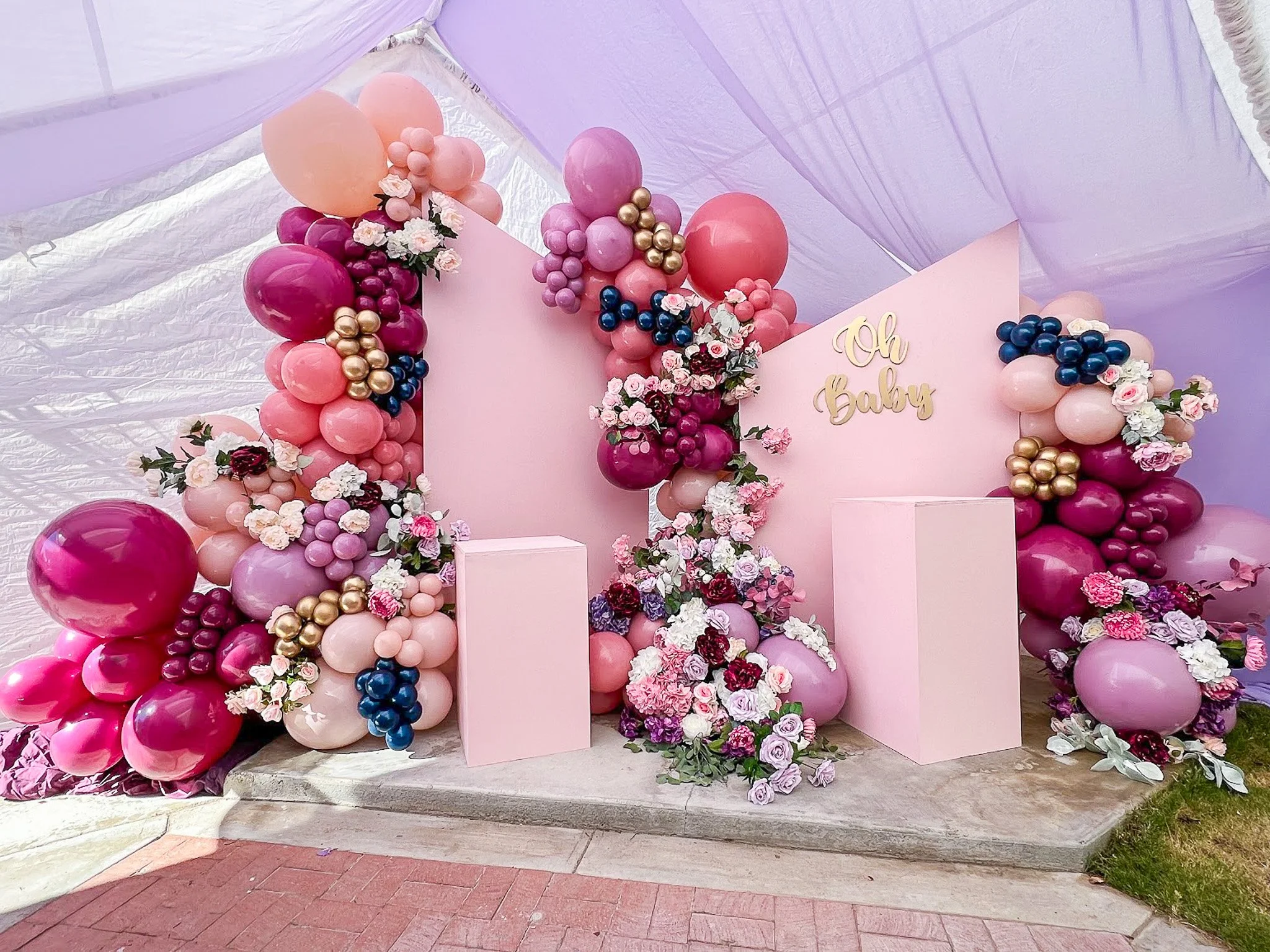 Pink and purple balloon arrangement with flowers and a sign that reads 'Oh Baby' for a gender reveal party or baby shower.