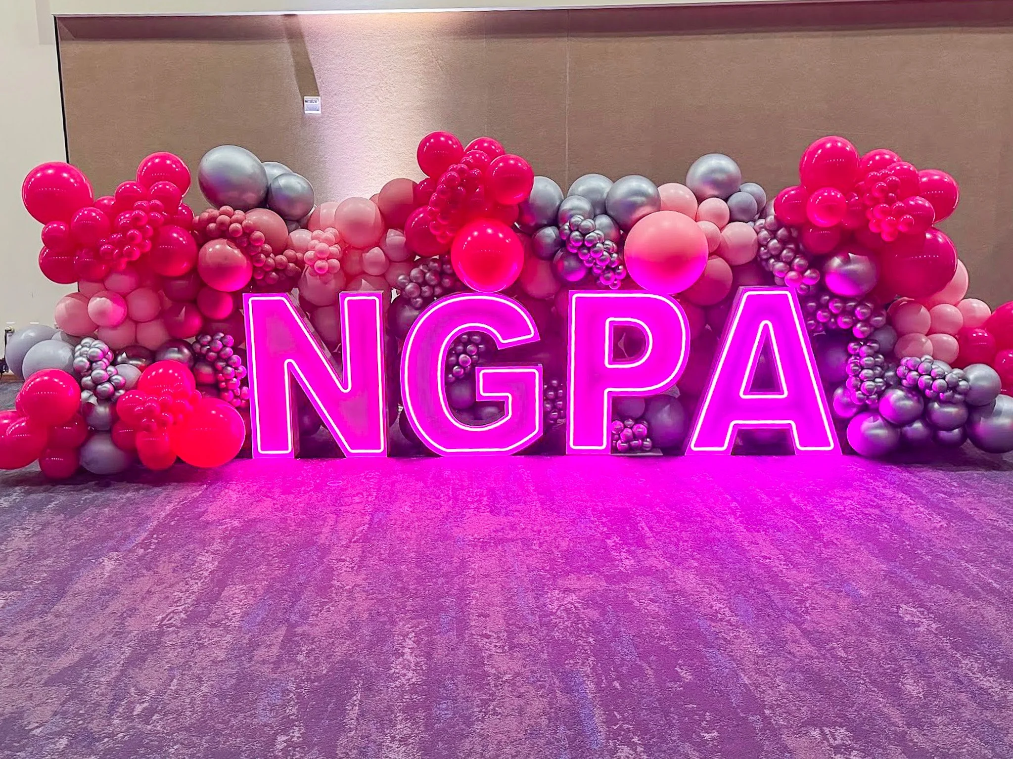 Pink, silver, and purple balloons arranged in a decorative display with illuminated neon pink letters.