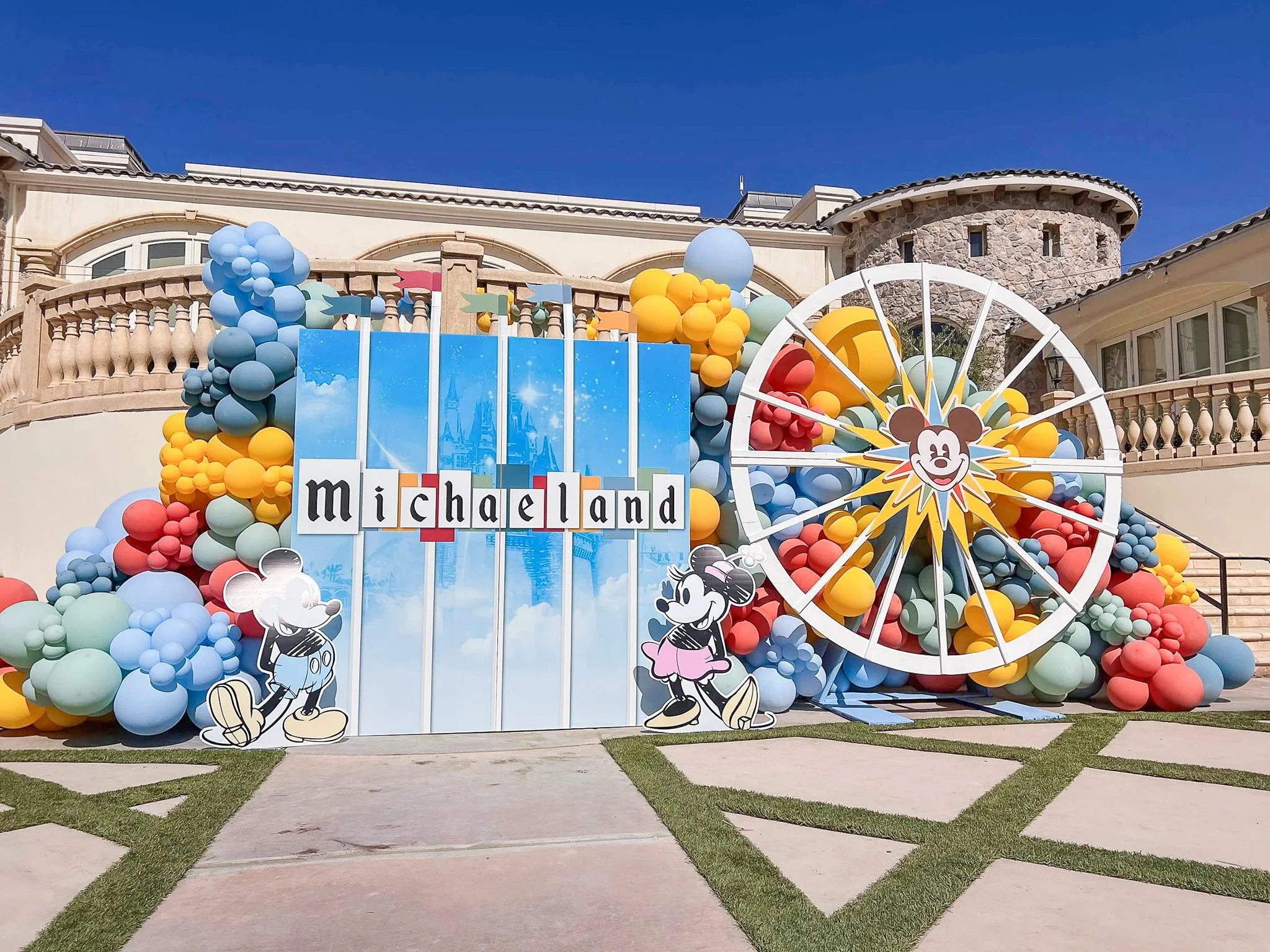 Decorative display with balloons, featuring a sign that says 'Michaeland', Mickey Mouse, Minnie Mouse, and related Disney-themed elements on a building backdrop.