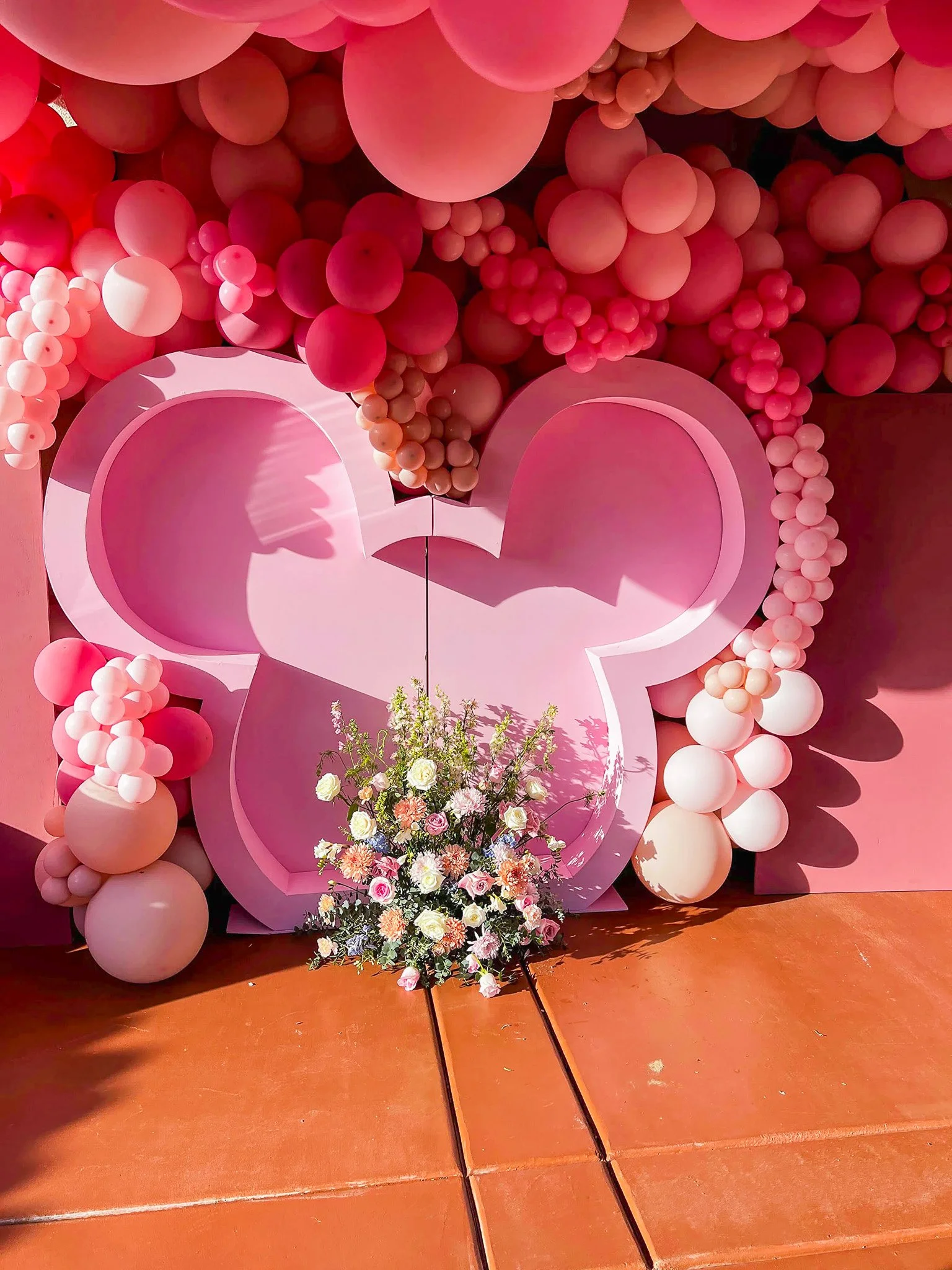 Pink heart-shaped display with balloons and flowers.