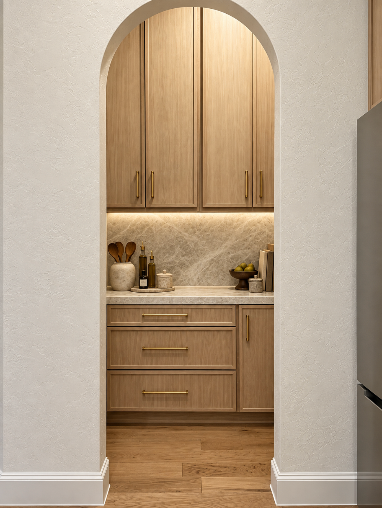 Tall arched opening framing warm wood built-in cabinetry, stone backsplash and integrated under-cabinet lighting.