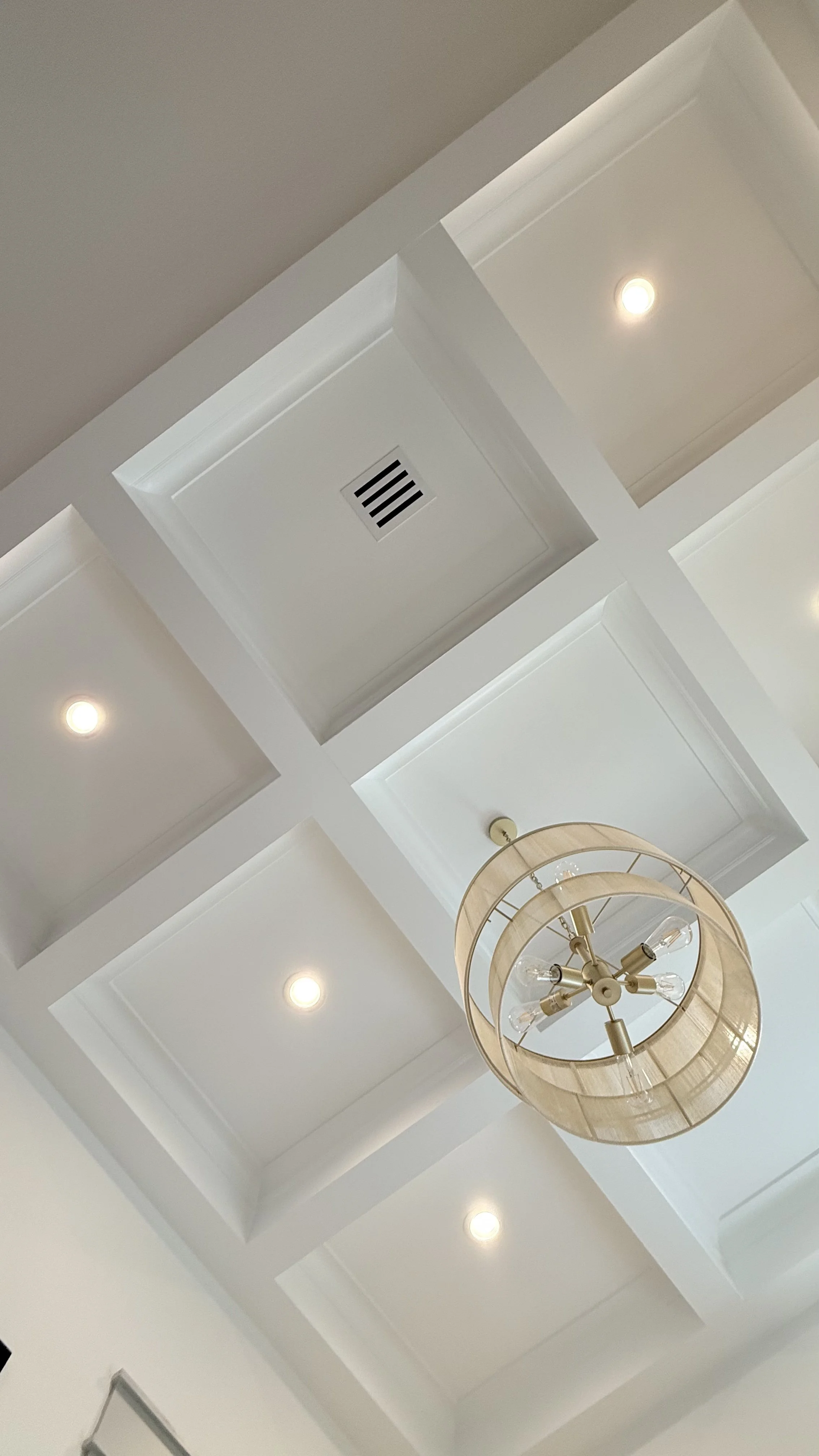 Upward view of a geometric coffered ceiling centered by a circular warm-metal lantern fixture.