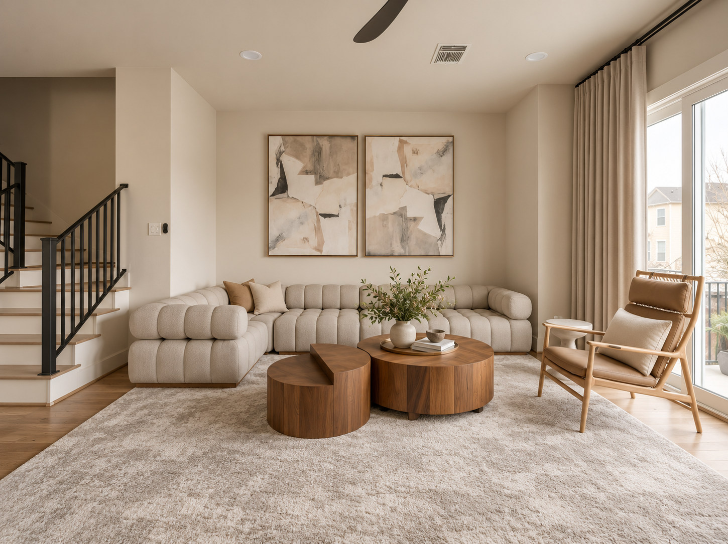 Neutral living room with curved sectional, round wood tables, abstract artwork and soft natural light