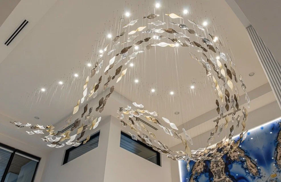Suspended metallic light installation with flowing ribbon-like forms and integrated points of light.