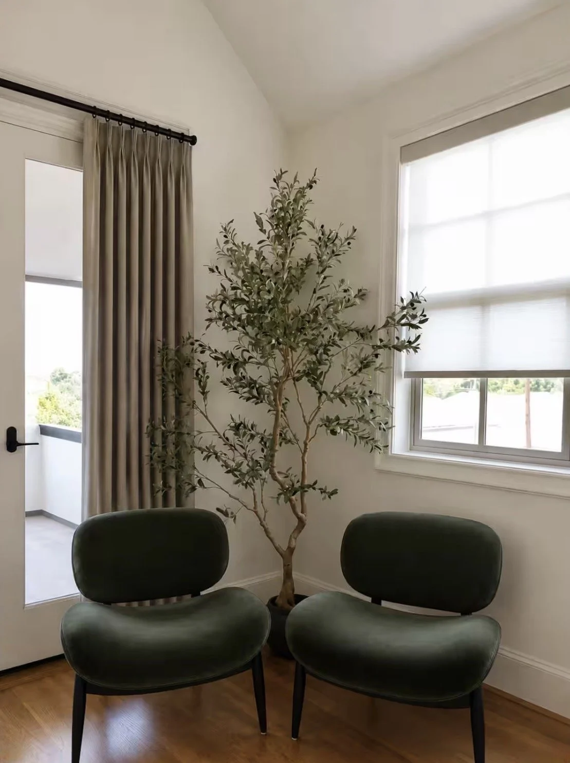Intimate sitting area with two green chairs, tall indoor tree and neutral window treatments