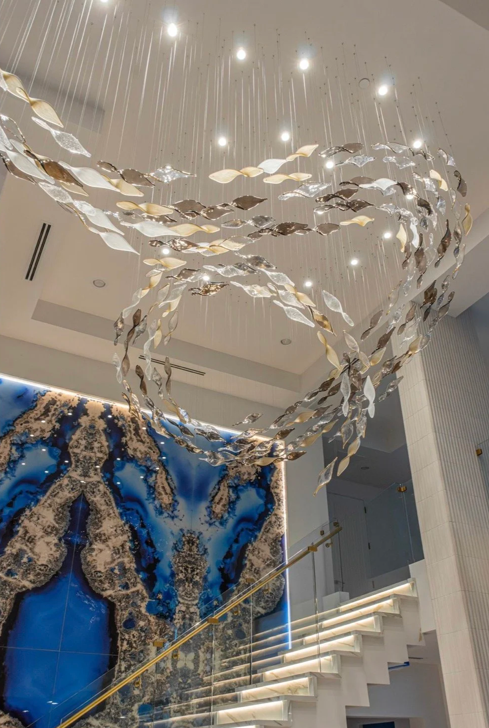 Close view of a suspended metallic ribbon sculpture with integrated lighting above a blue stone feature.