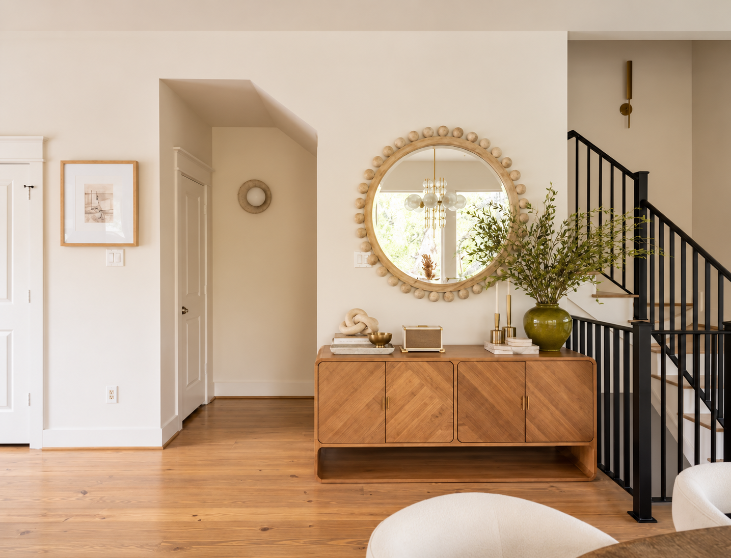 Bright entryway with wood console, round statement mirror, floral arrangements and black stair railing
