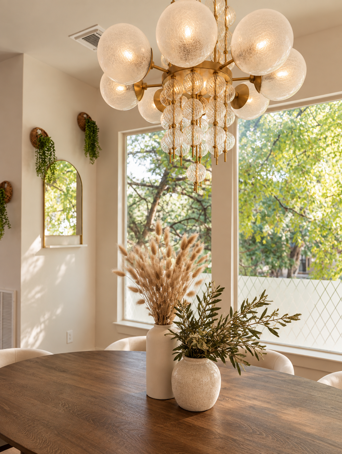 Bright dining area with statement chandelier, round table, large windows and botanical accents