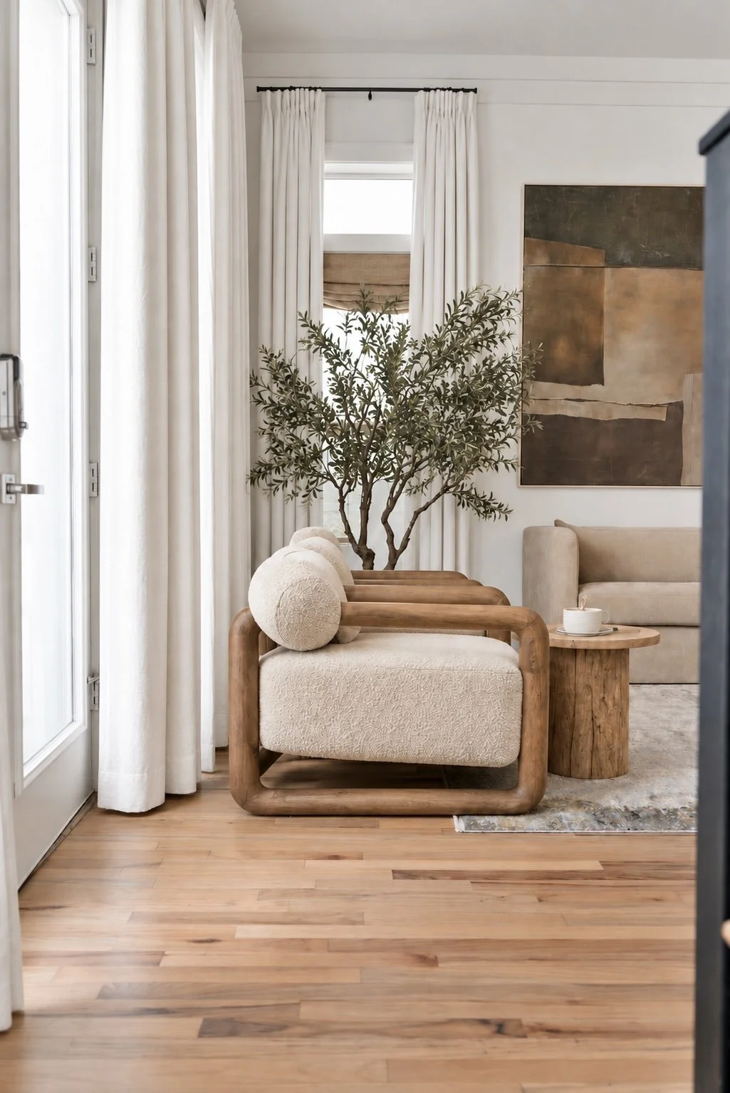 Sunlit lounge corner with bouclé seating, sculptural wood furniture, olive tree and abstract artwork.