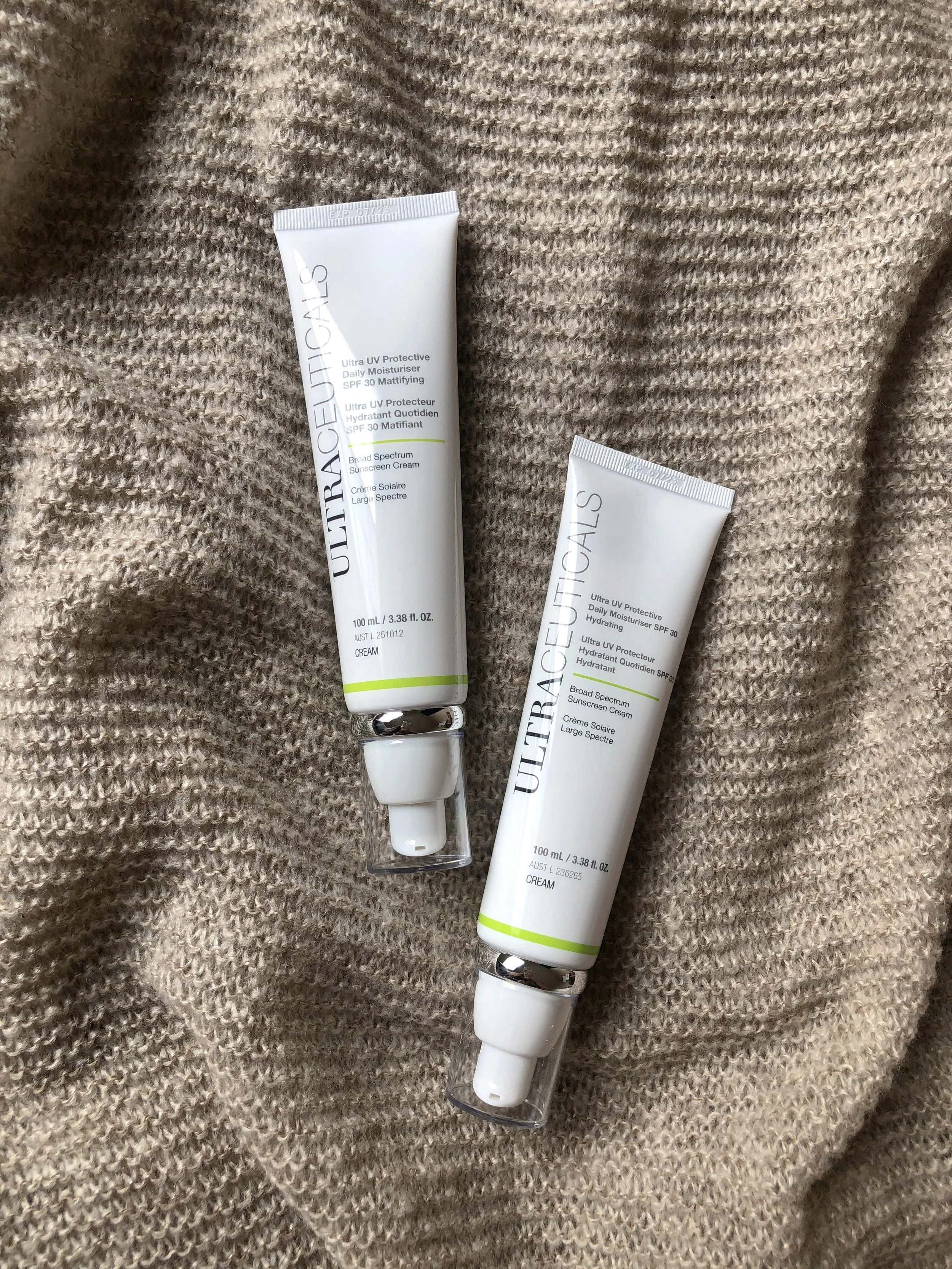 Twee tubes van Ultraceutical zonnebrandcrème op een zachte, beige gebreide stof.