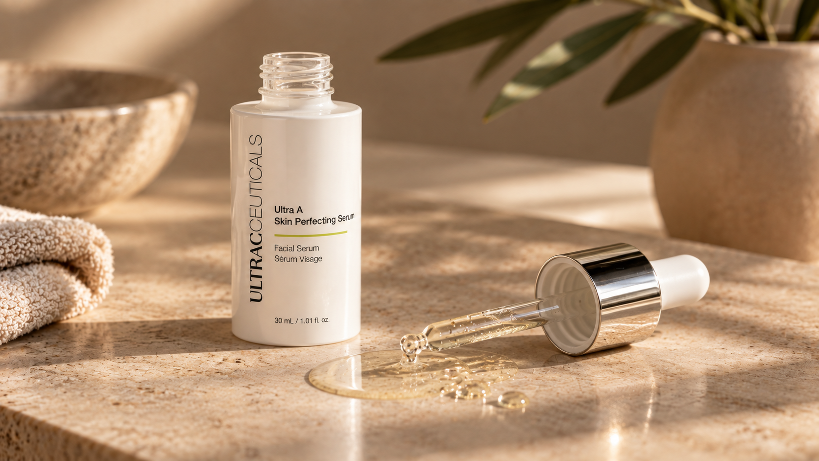 Een flesje Ultra A Skin Perfecting Serum met een pipet dat serum over een marmeren oppervlak druppelt, met een beige handdoek en een plantenpot op de achtergrond.