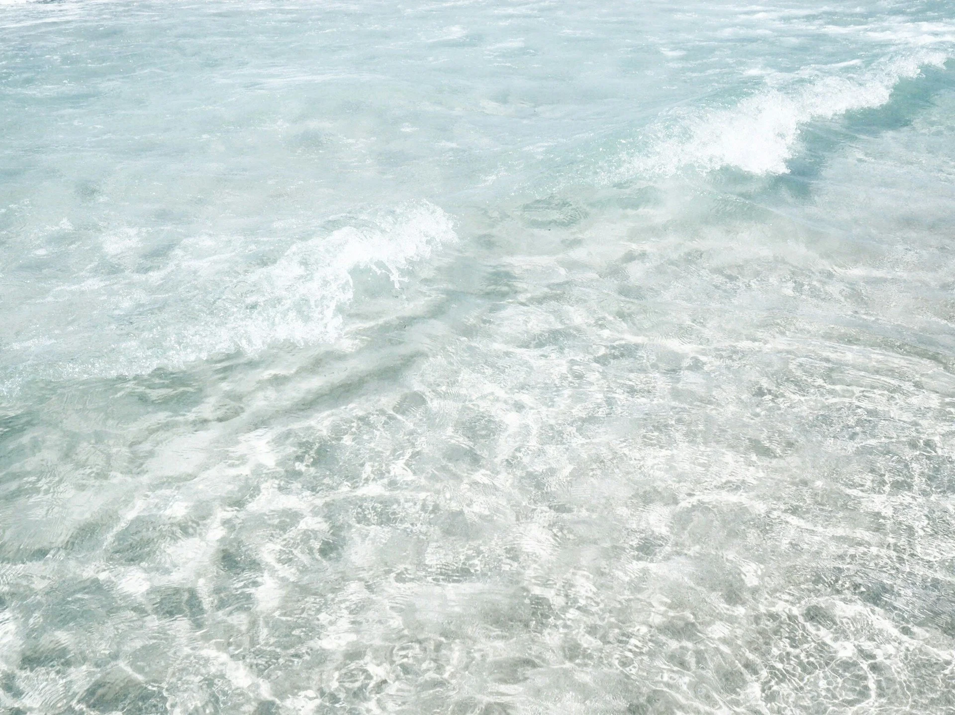 Clear ocean water with gentle waves and foam near the shoreline.
