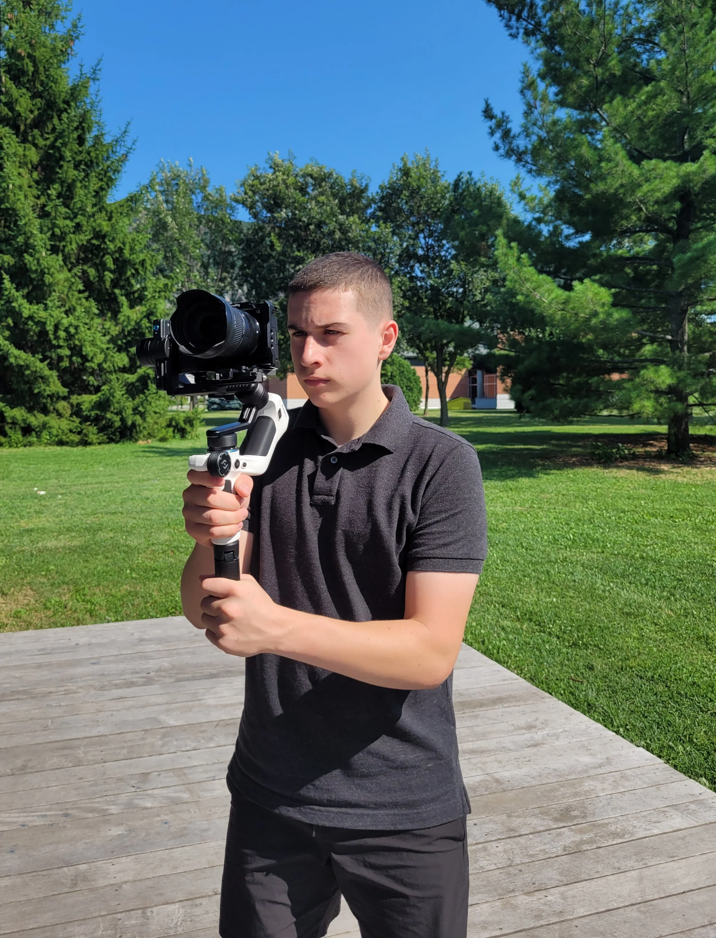 Jeune homme observant à travers un télescope en plein air dans un parc avec des arbres et un ciel ensoleillé.