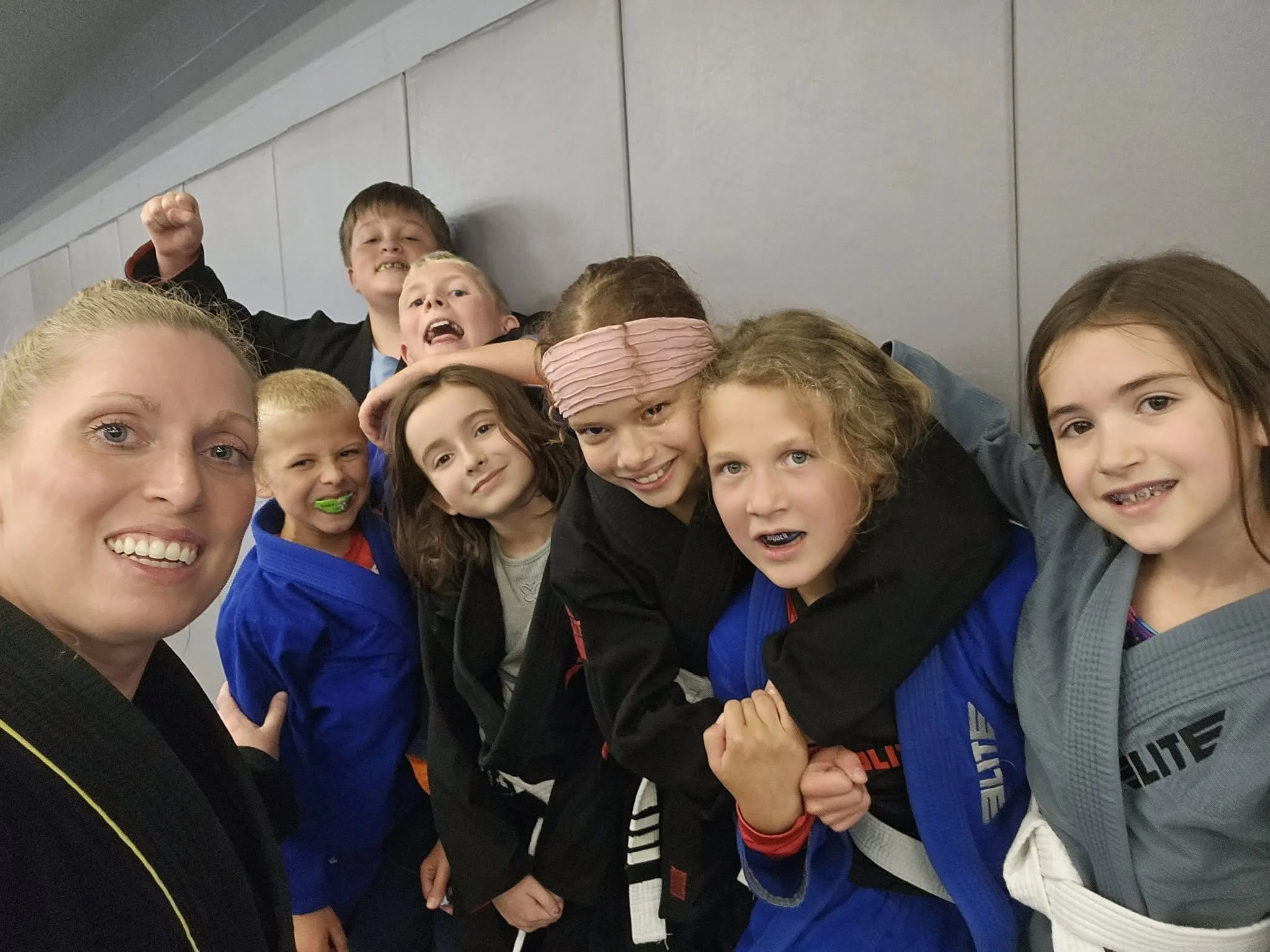 A group of children and a woman taking a selfie together, showing smiles and expressions of happiness and excitement.