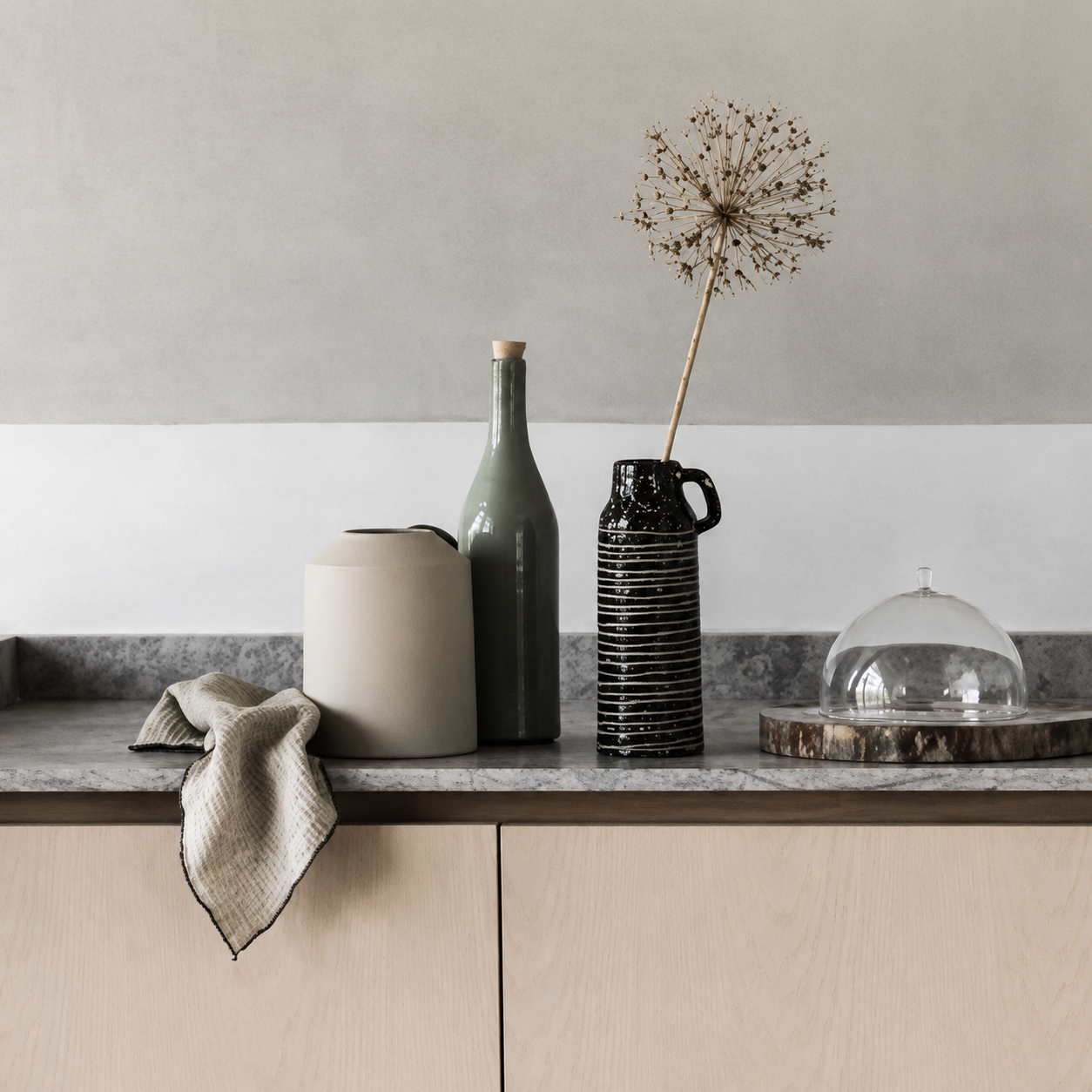 Decorative kitchen arrangement with vases, a cloth, and a glass dome on a marble countertop.