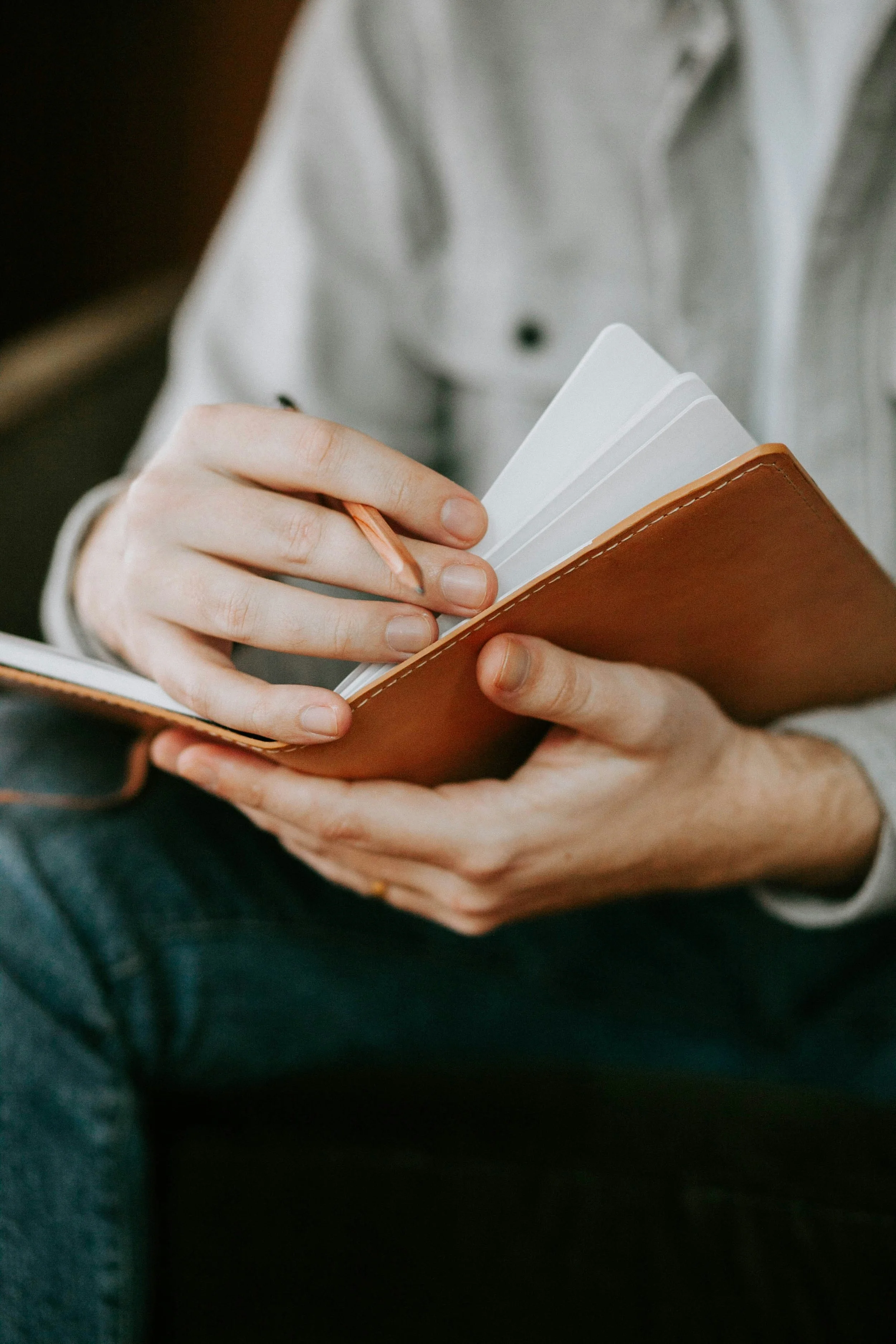 Person holding a brown leather notebook and writing with a pen.
