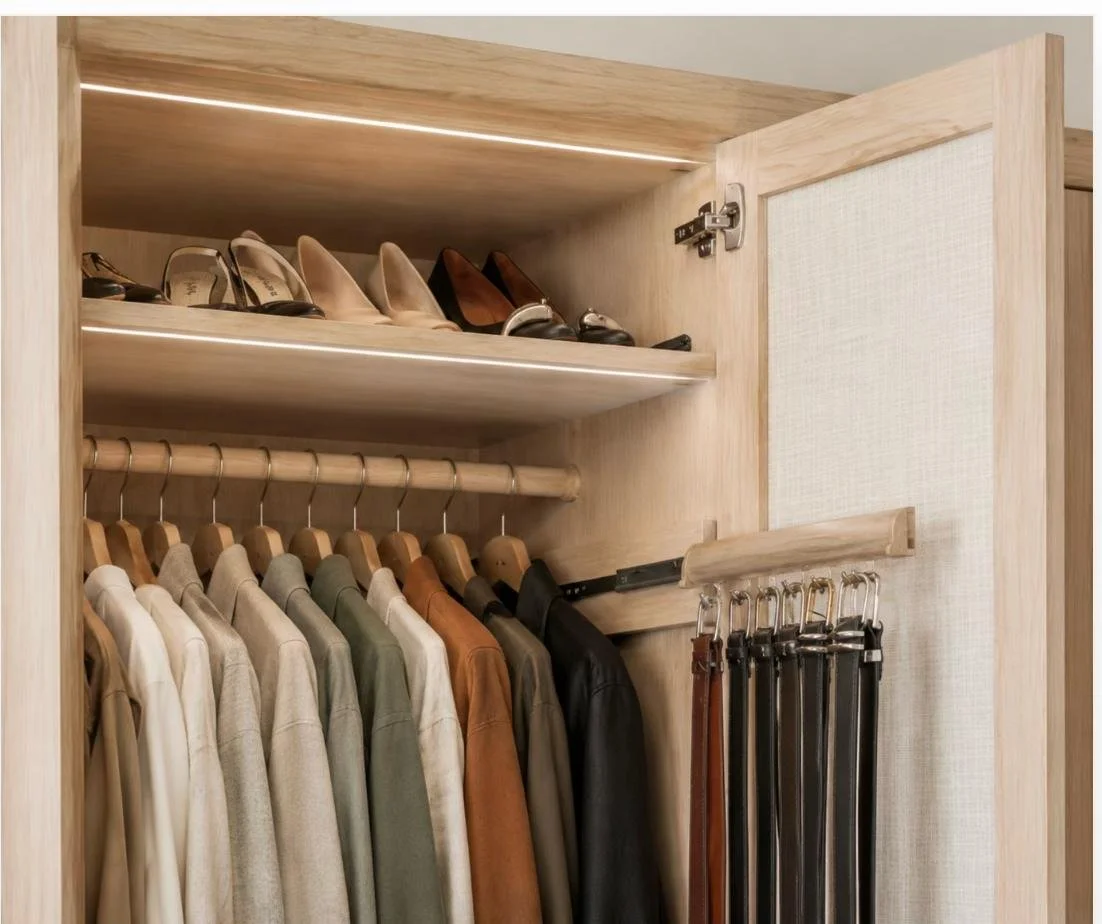 A wooden wardrobe with hanging shirts, a shelf with high heels, and belts hanging on a hook.