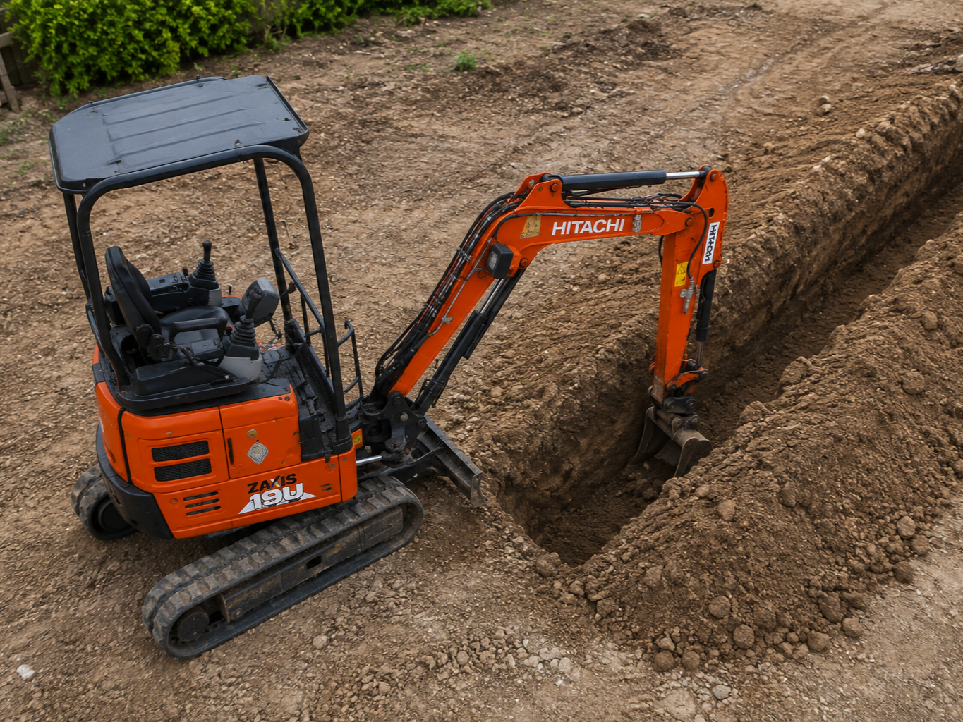 Orange mini excavator digging a trench in dirt at a construction site.