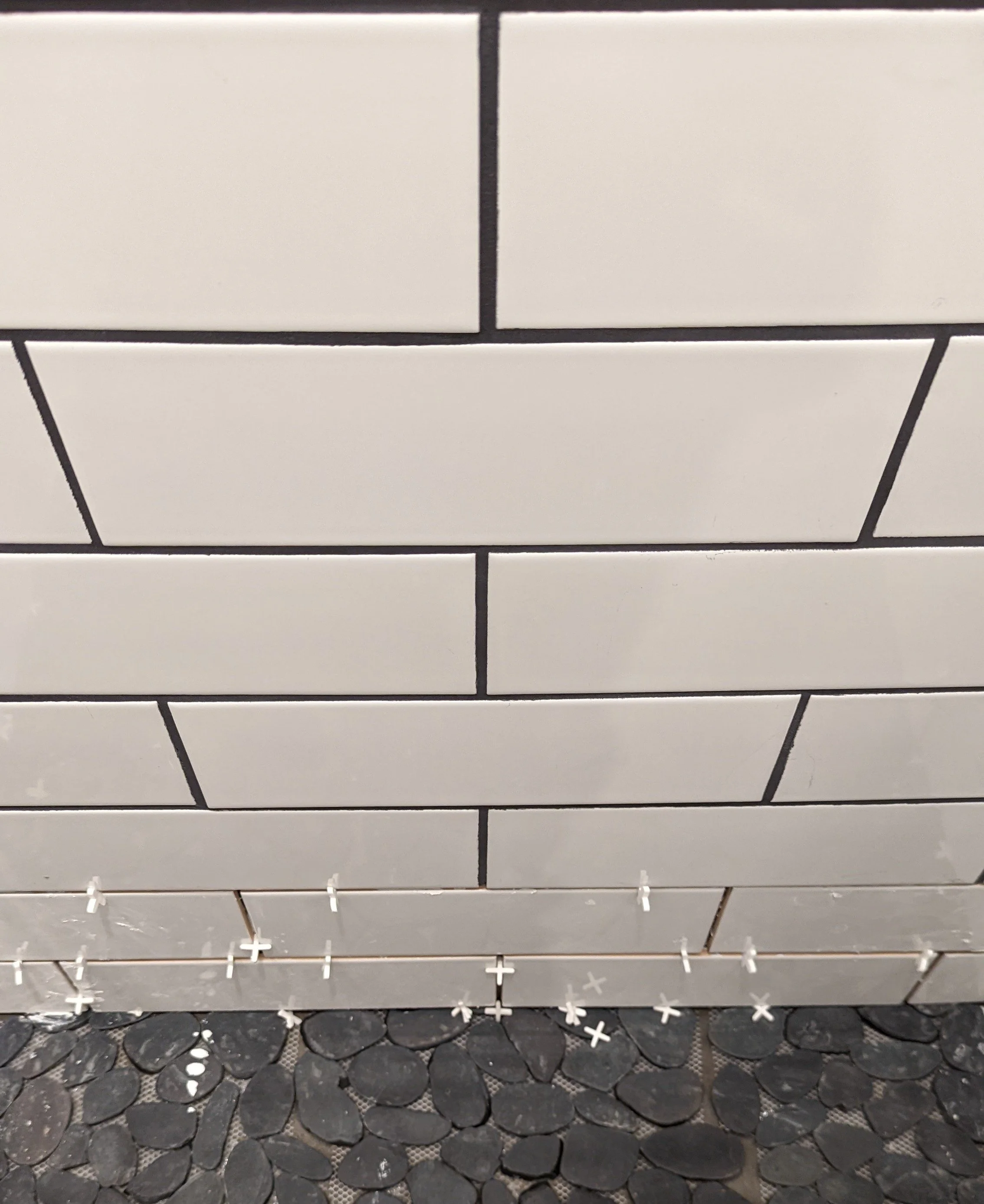 Empty white metal retail display rack with multiple shelves, situated over a black pebble-textured floor.