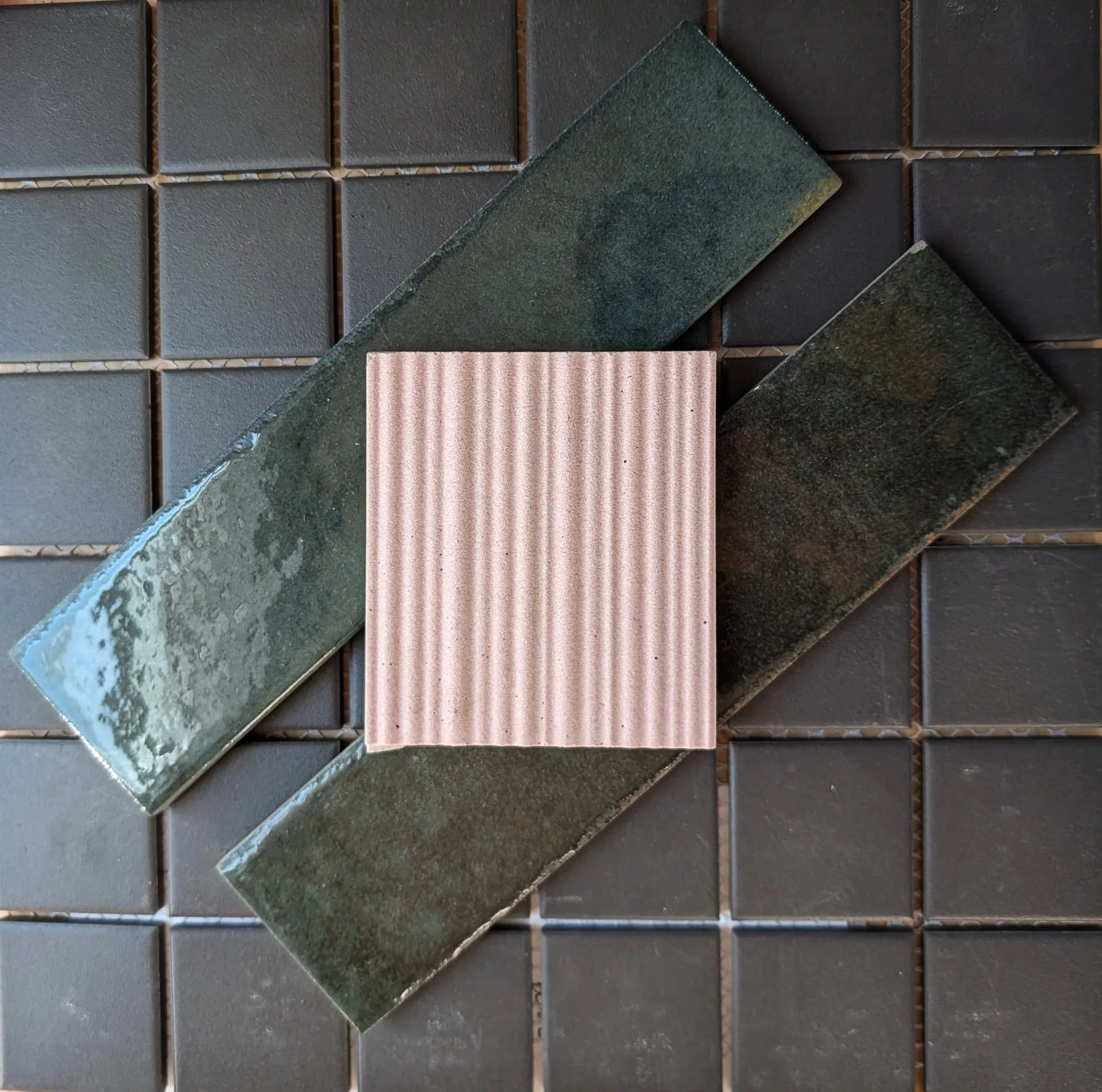Close-up view of various types of tiles including square and rectangular tiles in shades of dark gray, green, and beige, arranged on a surface.