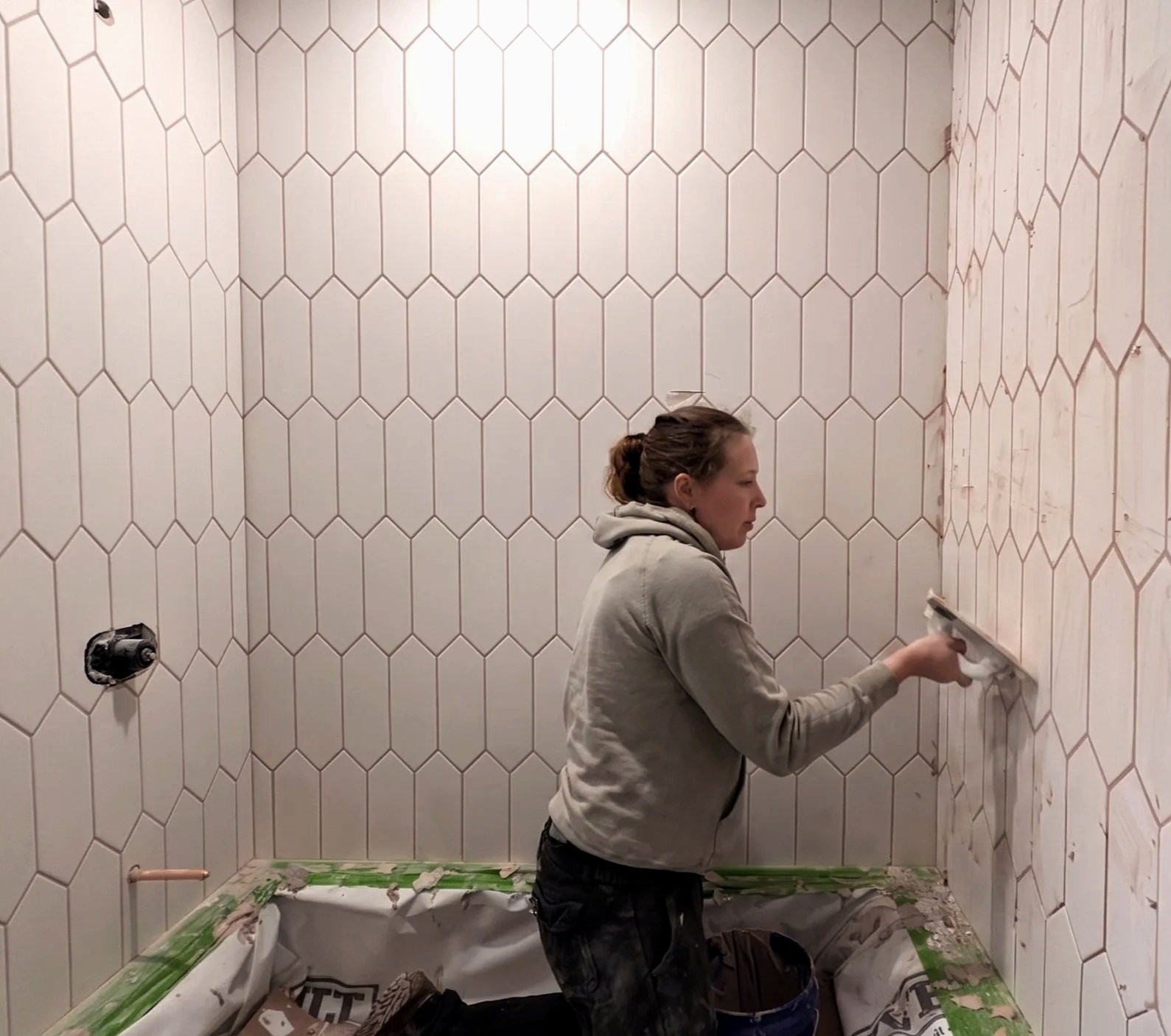 A woman installing white hexagonal tiles on a wall in a bathroom.