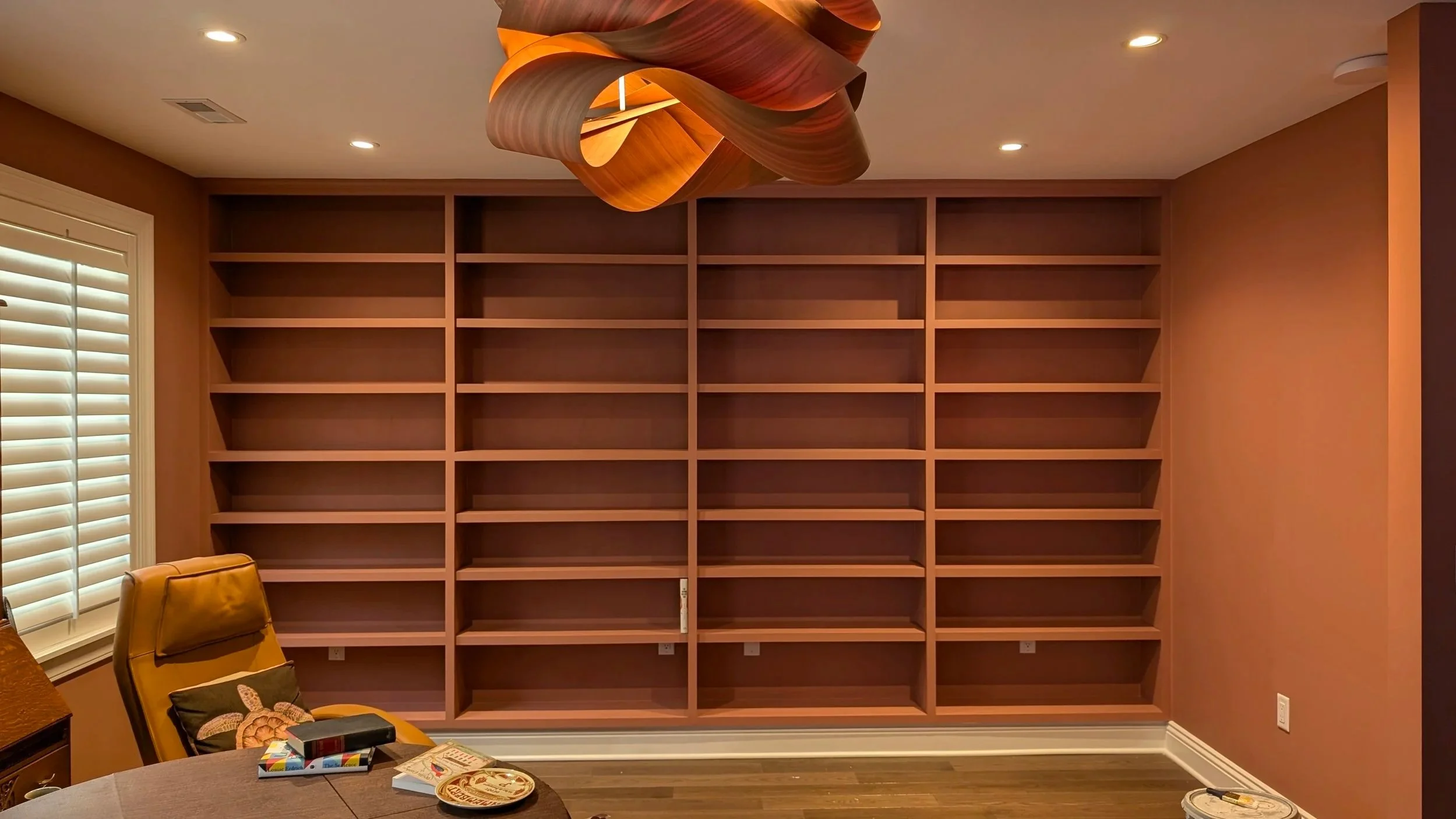 Empty wooden bookshelf on a wall in a room with recessed ceiling lights.