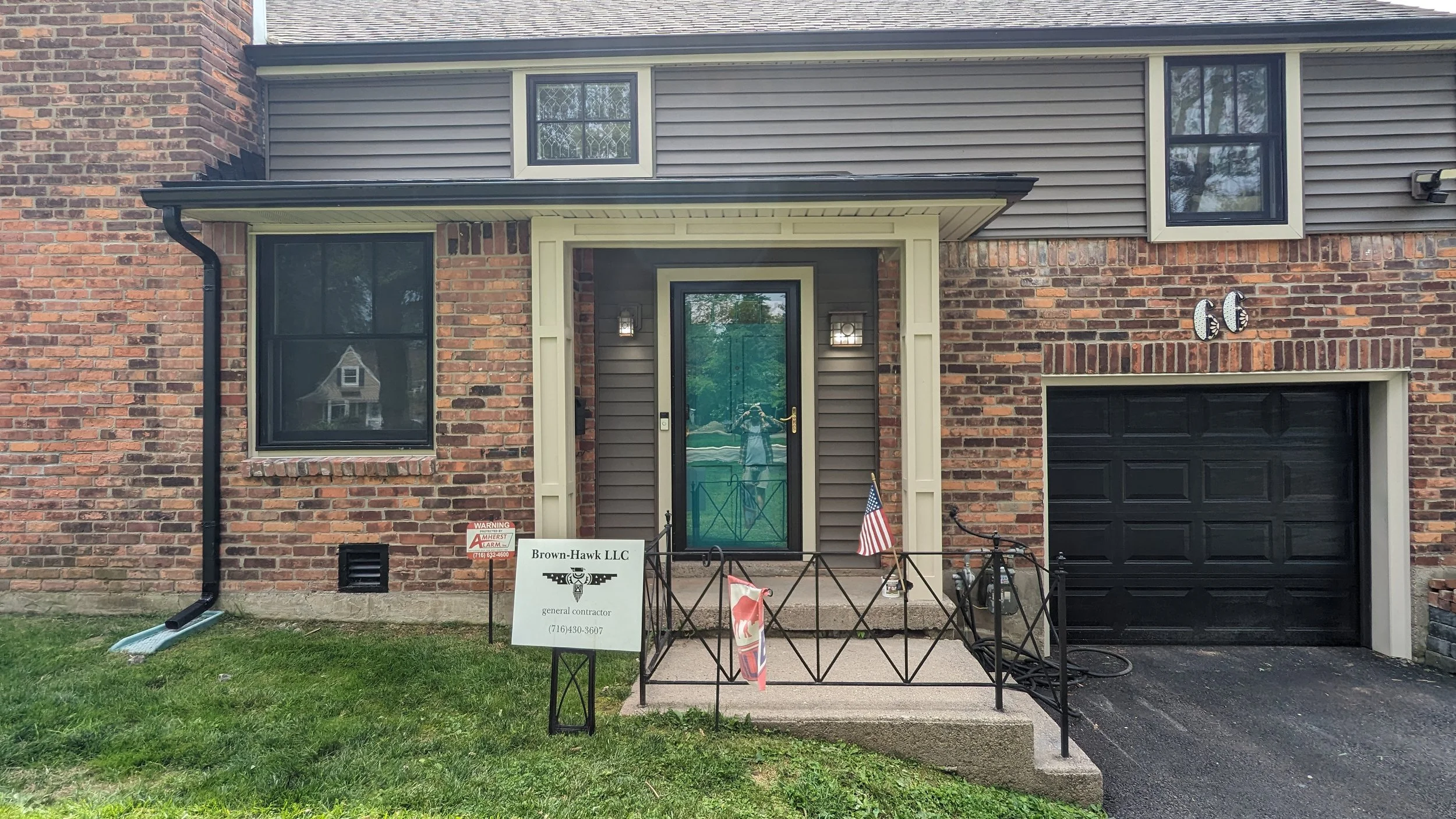 Brick and siding residential house with attached garage, front door, and porch. House number 66 displayed on wall. Sign for Brown-Hawk LLC general contractor on front lawn.