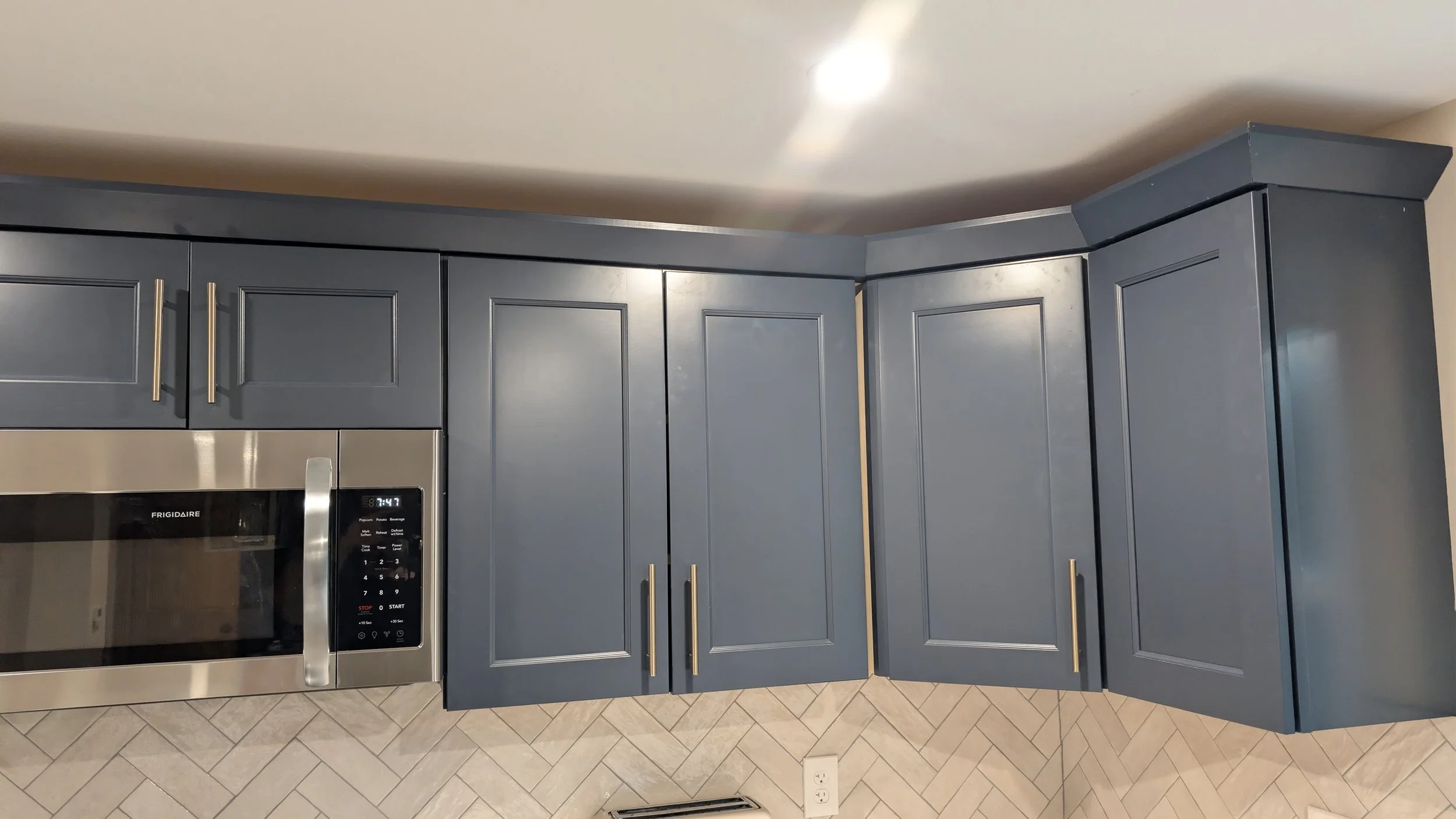 Blue kitchen cabinets with long silver handles, a stainless steel microwave oven, tiled floor, and a white ceiling.