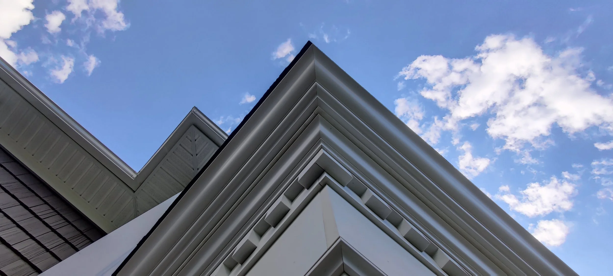Close-up of the corner of a modern building with geometric architectural details, against a blue sky with scattered clouds.