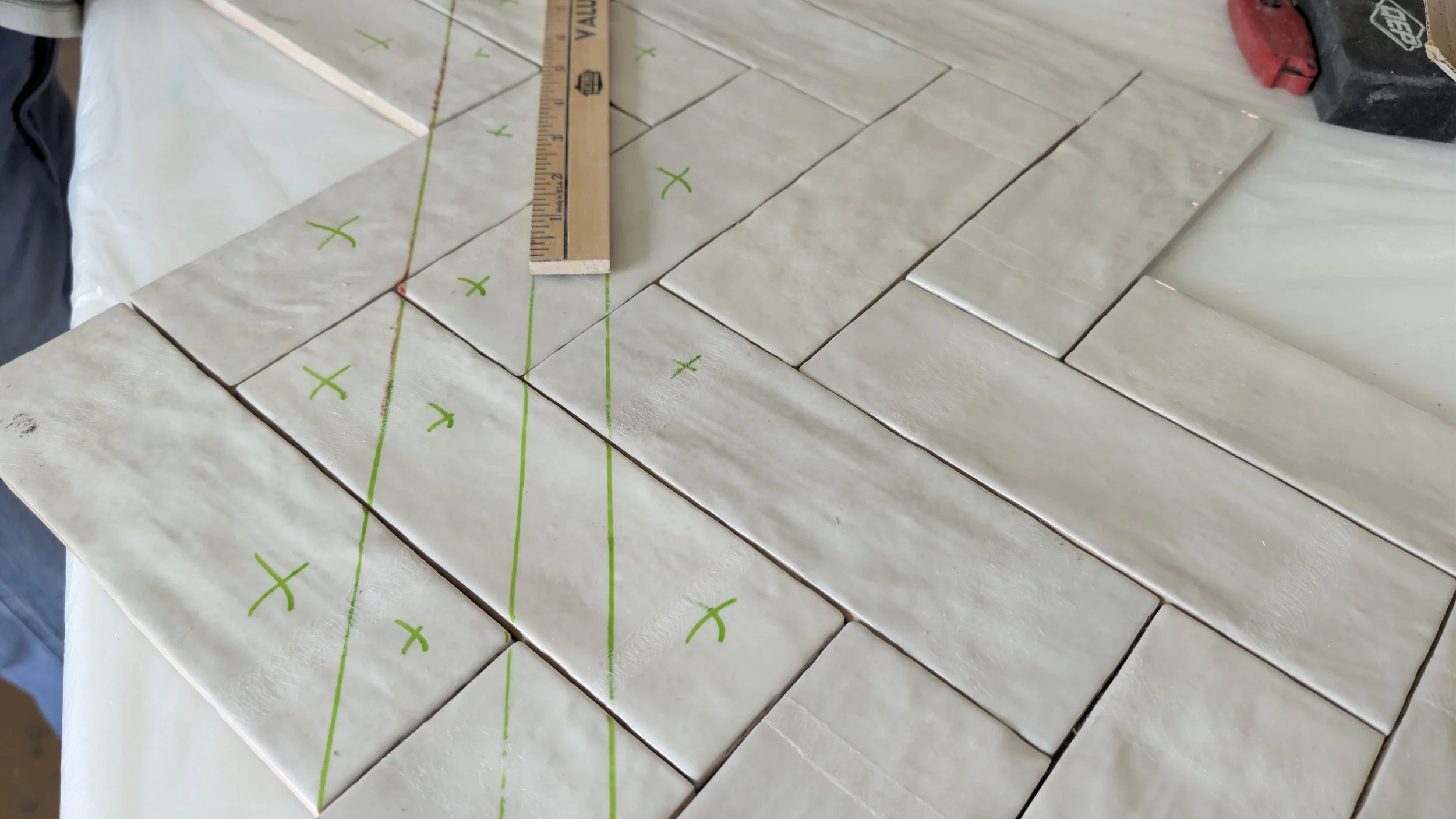 Tile installation process with square tiles laid out on a surface, marked with green markings and lines for alignment, and a wooden ruler measuring the layout.