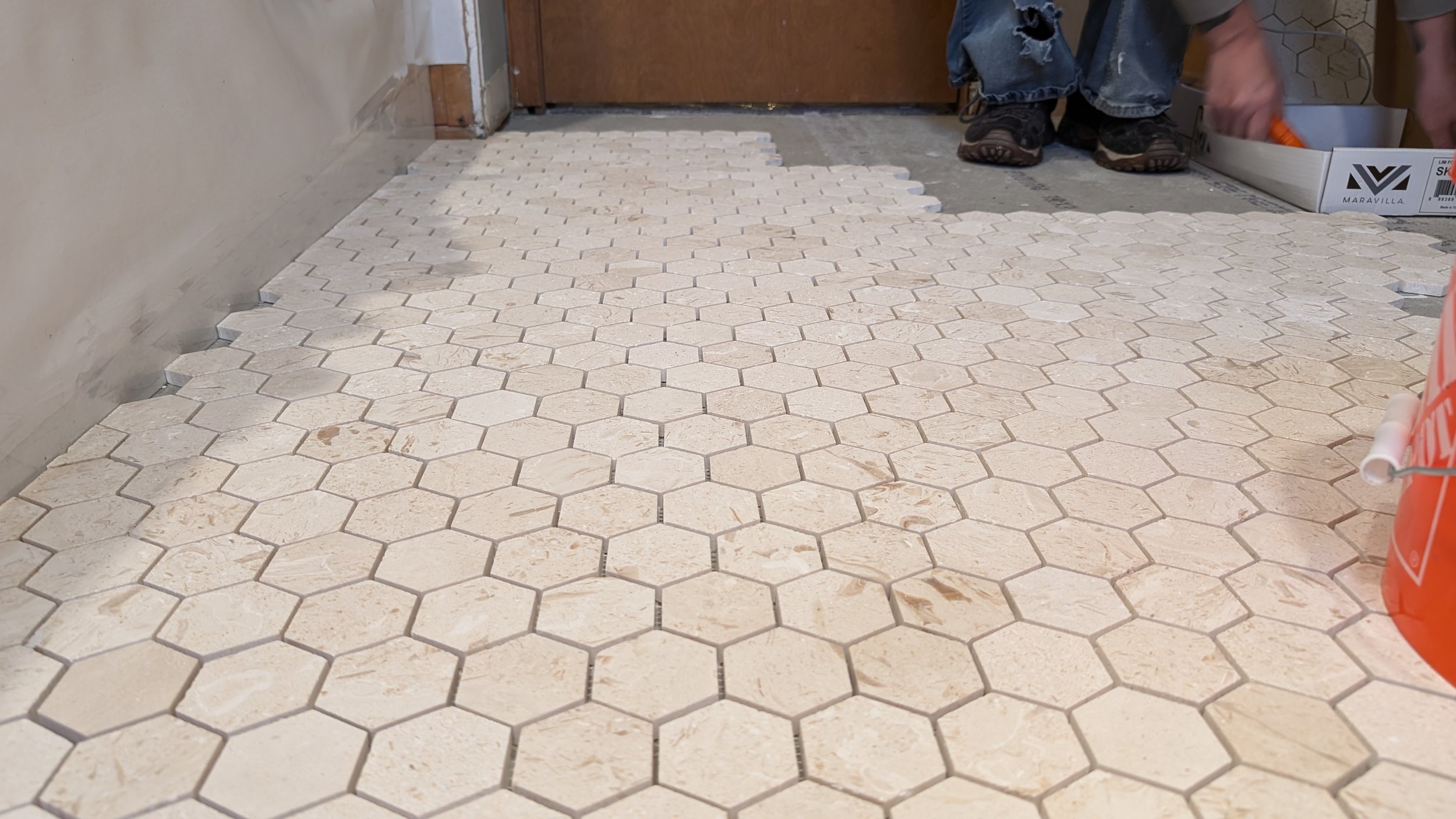 A person installing hexagonal tile flooring in a room, with some tiles already placed and others being adhered.