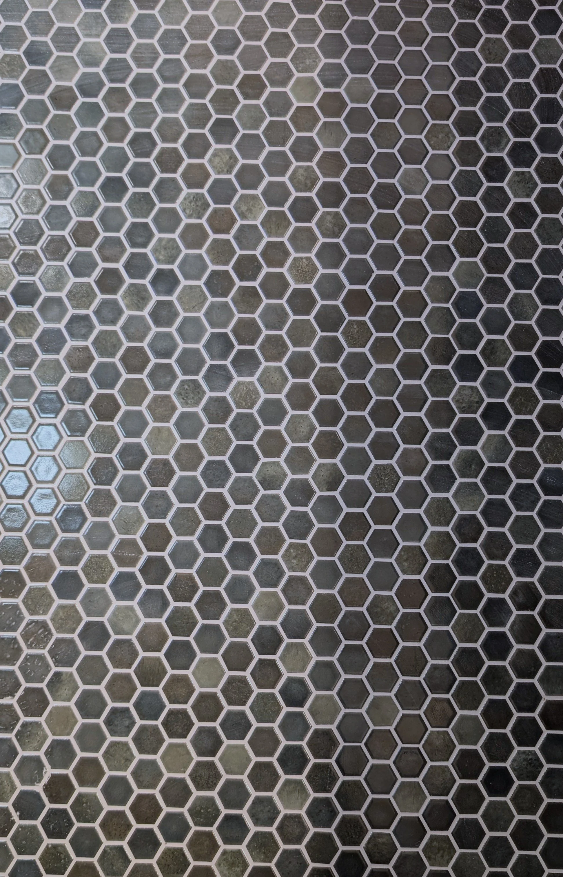Close-up of a floor with hexagonal tiles in various shades of gray, separated by white grout lines.