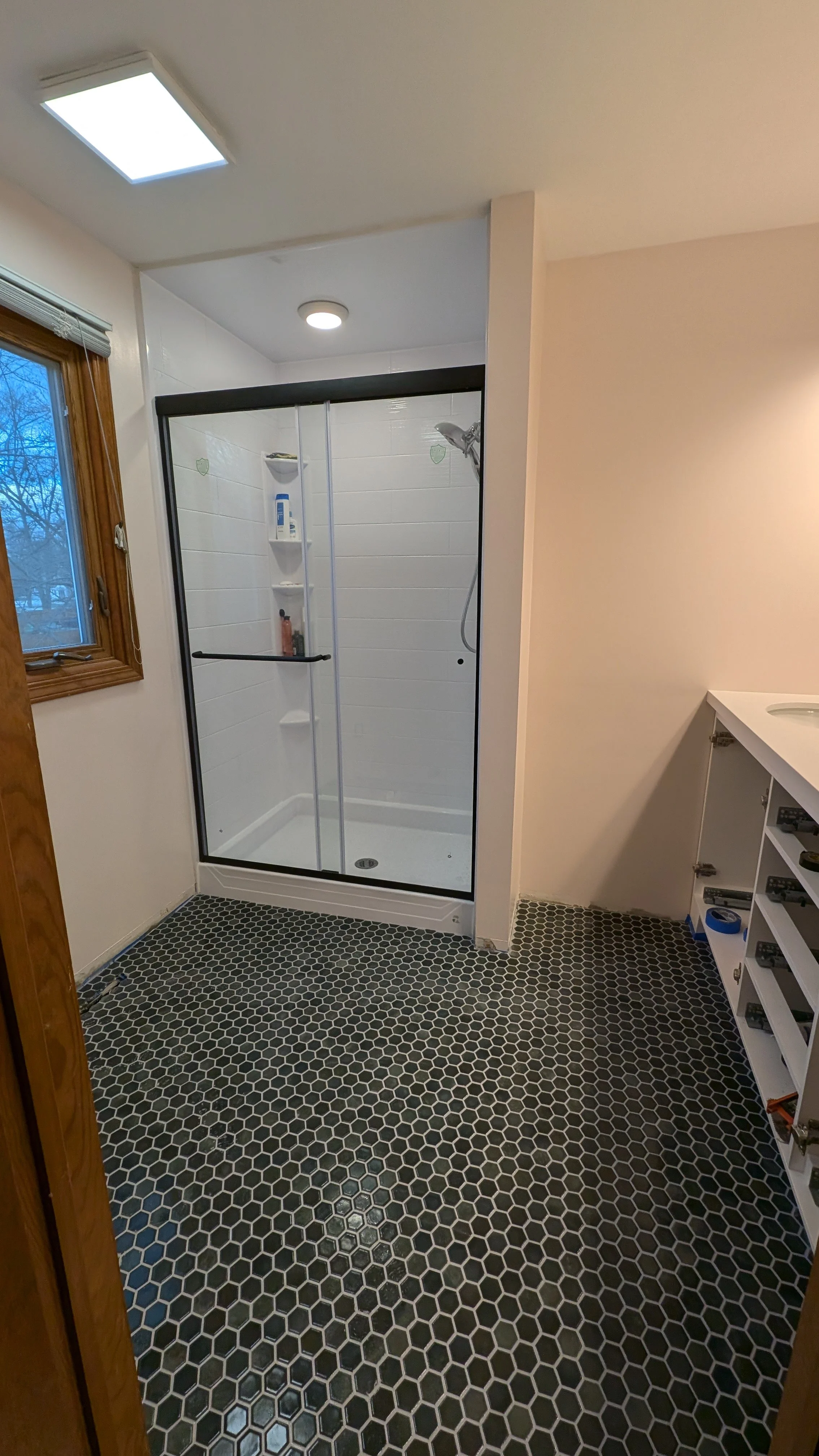 Bathroom with black hexagon tile floor, glass shower enclosure, and white vanity with open shelves.
