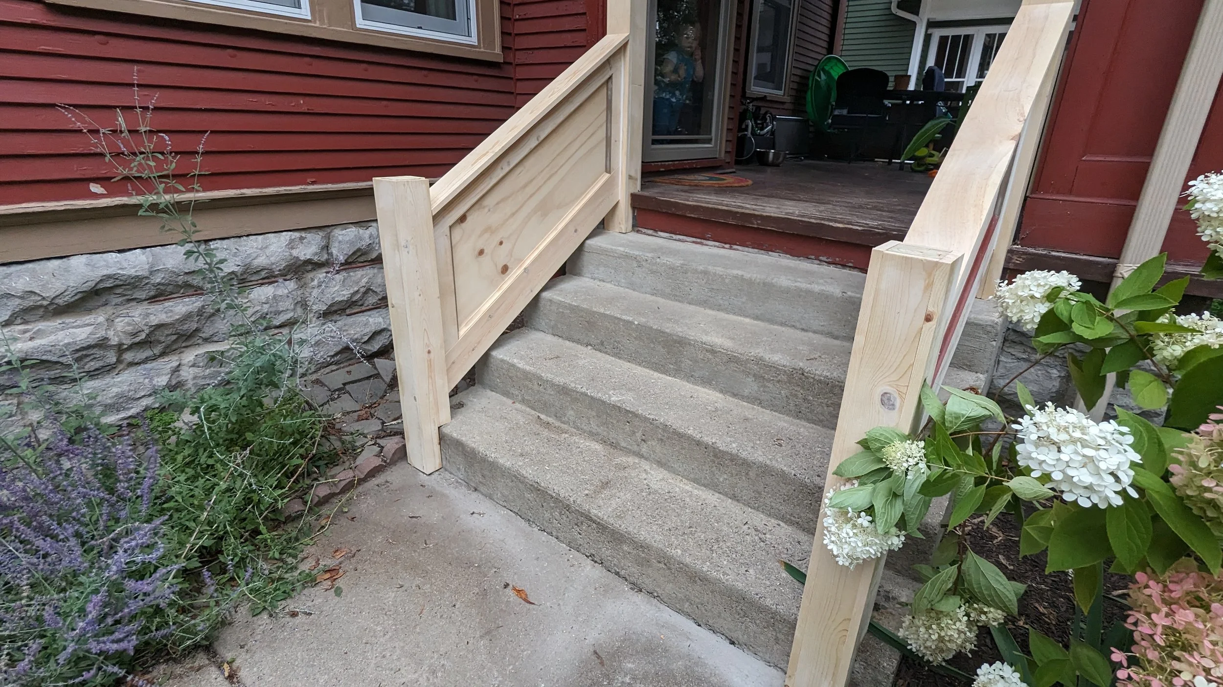 Wooden handrails are being installed on a concrete staircase leading to a house's porch.
