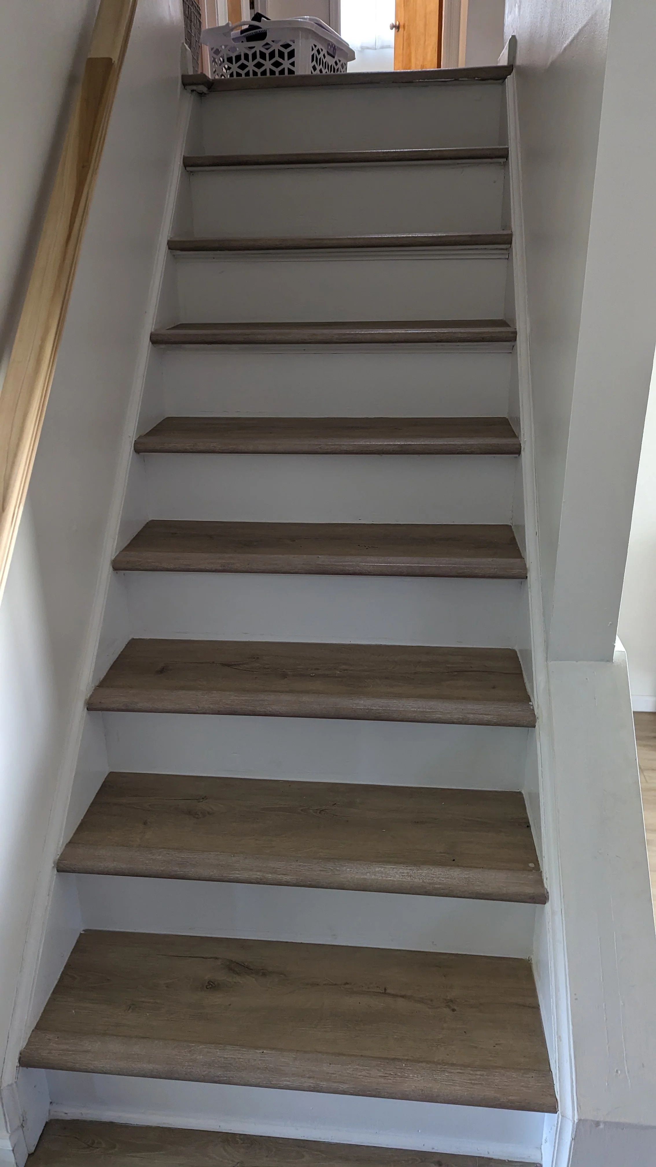 A staircase with wooden treads and white risers leading up to a doorway with a view of a laundry basket on the top step.