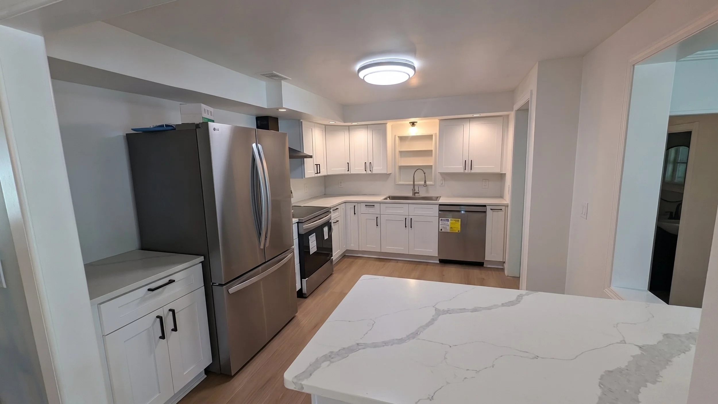 Modern kitchen with white cabinets, stainless steel appliances, a marble countertop, and wood flooring.