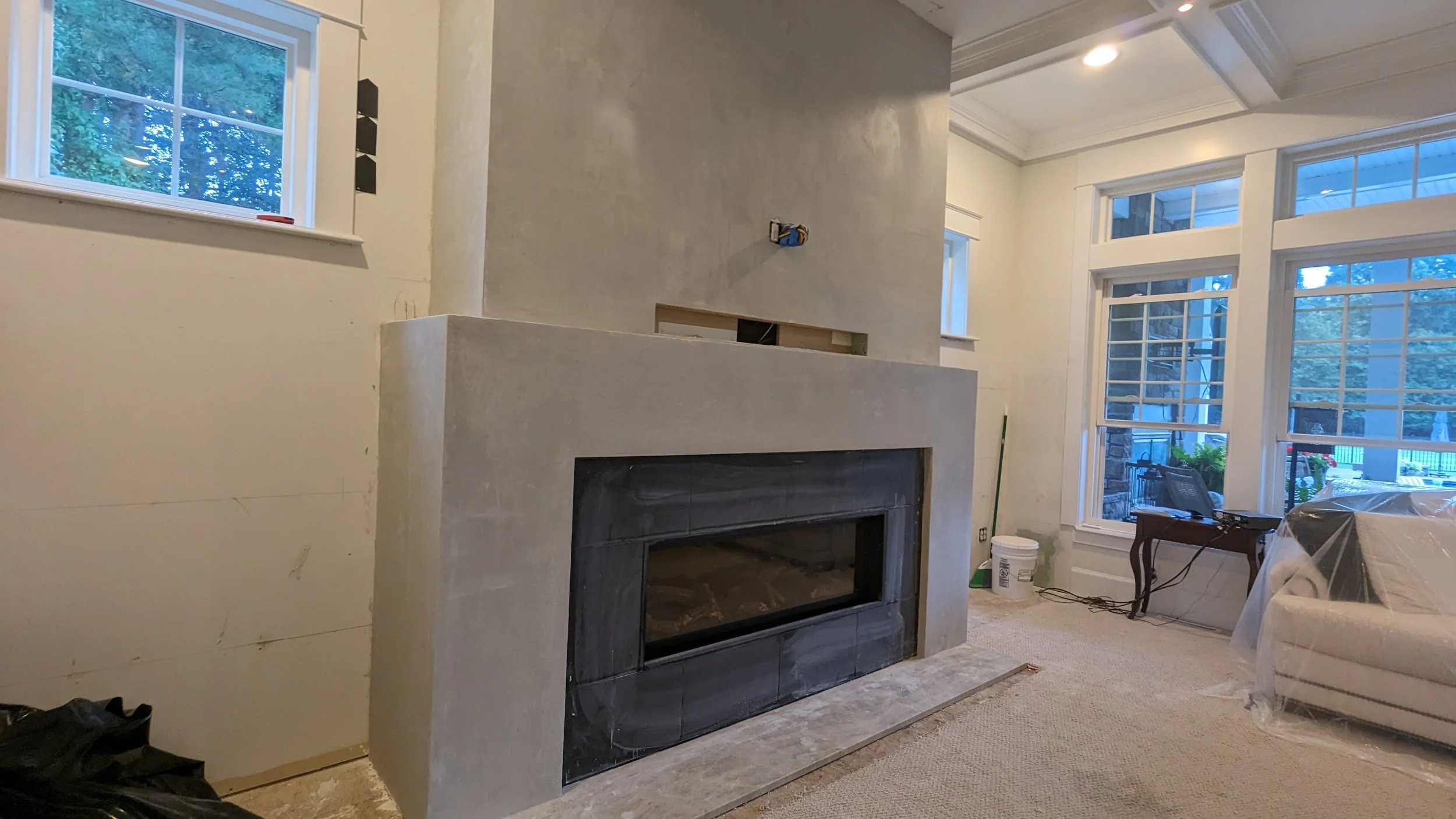 Living room with large windows, a gray fireplace, and ongoing construction or renovation work.