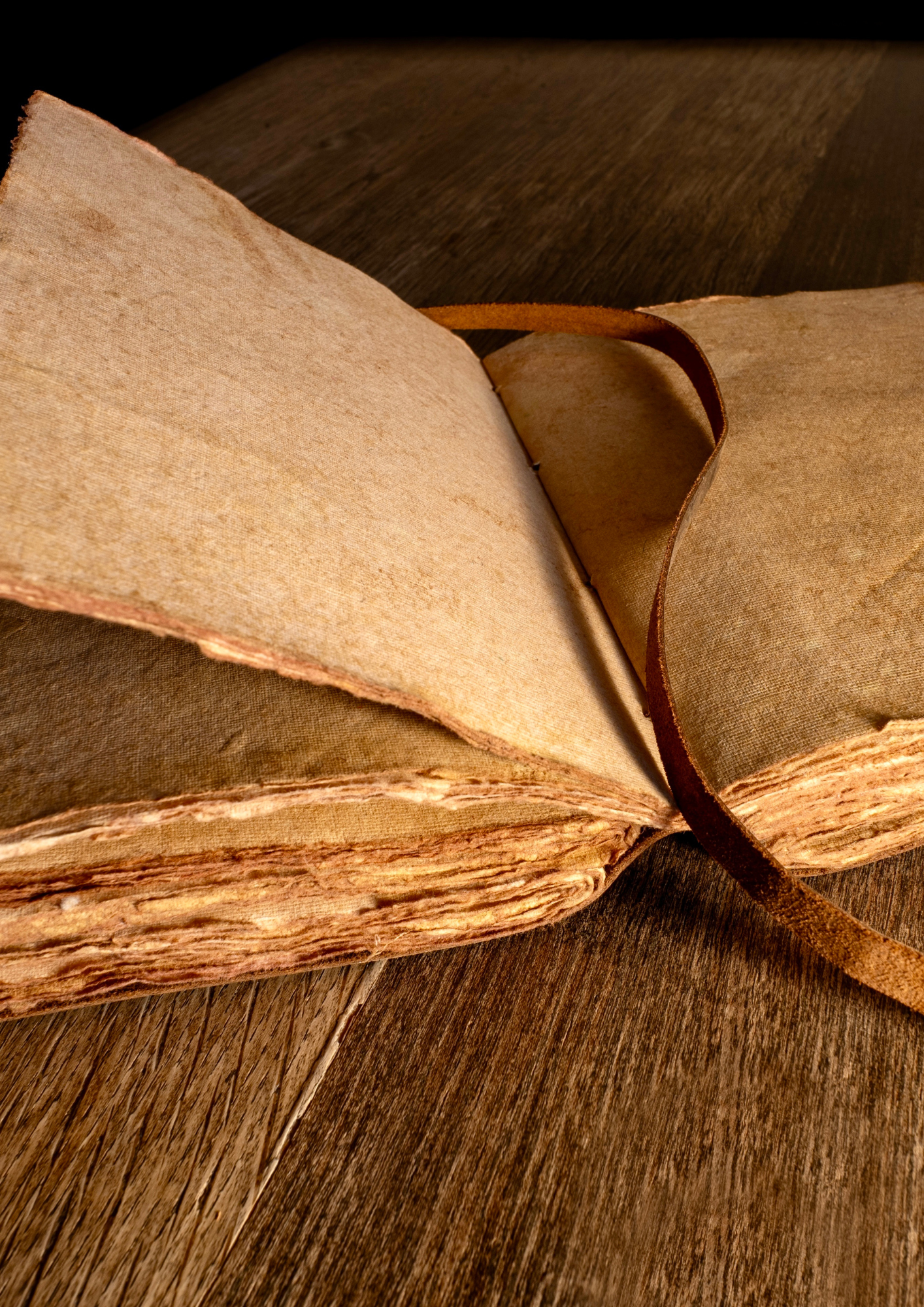 Ein offenes, altes Buch mit gelblichen, zerfransten Seiten auf einem dunklen Holzschreibtisch