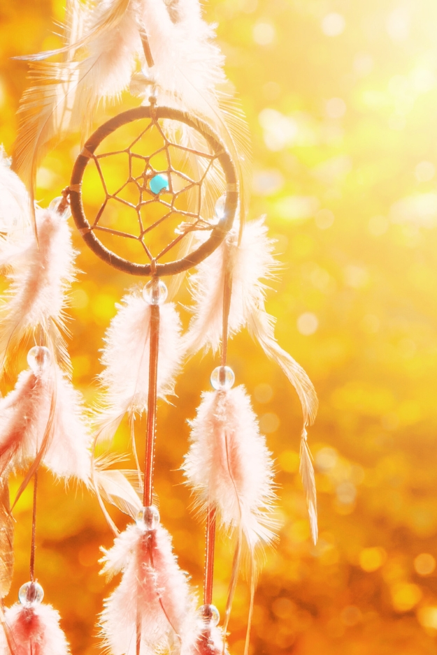 für Hypnose QHHT und tiefe therapeutische Begleitung in Lebenskrisen im Soul Spa BerlinNahaufnahme eines Traumfängers mit Federn und Perlen, im Sonnenlicht mit goldener Hintergrundbeleuchtung.